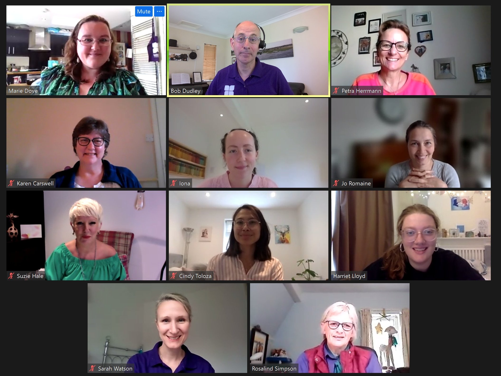 A Zoom call with twelve people smiling at their webcams, each in a separate window with various backgrounds visible.