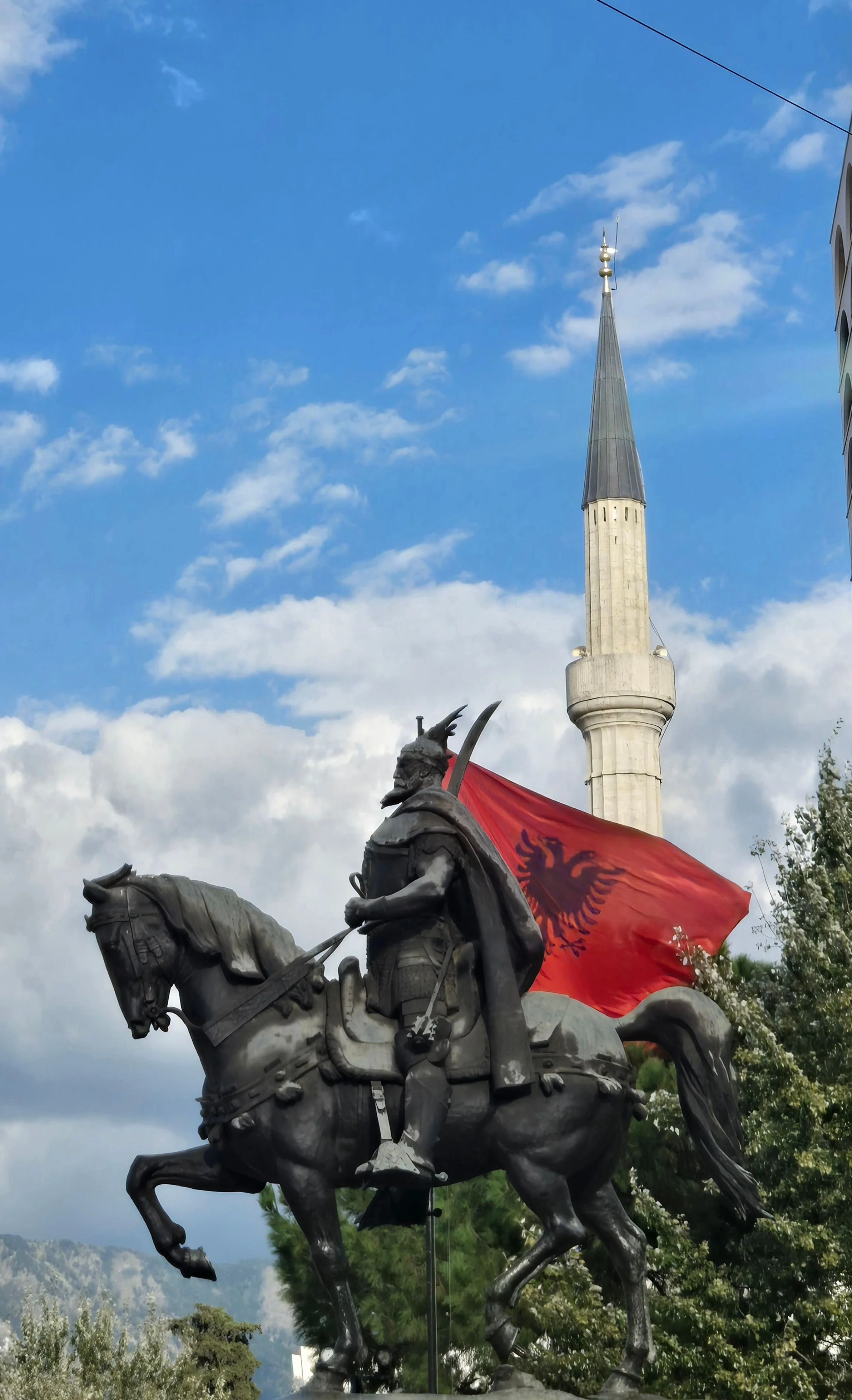 Skanderbeg Monument in Tirana, Albania, with the Albanian flag and Et’hem Bey Mosque in the background.