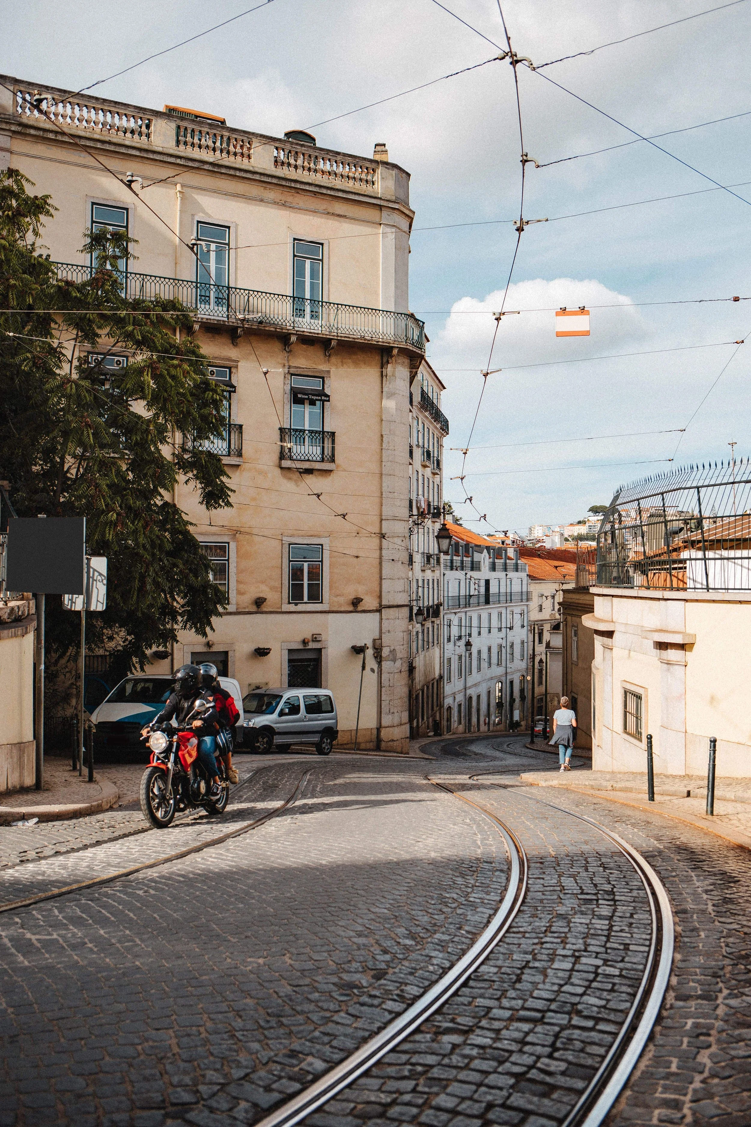 Hilly cobblestone street with tram tracks and historic buildings in Lisbon, Portugal.