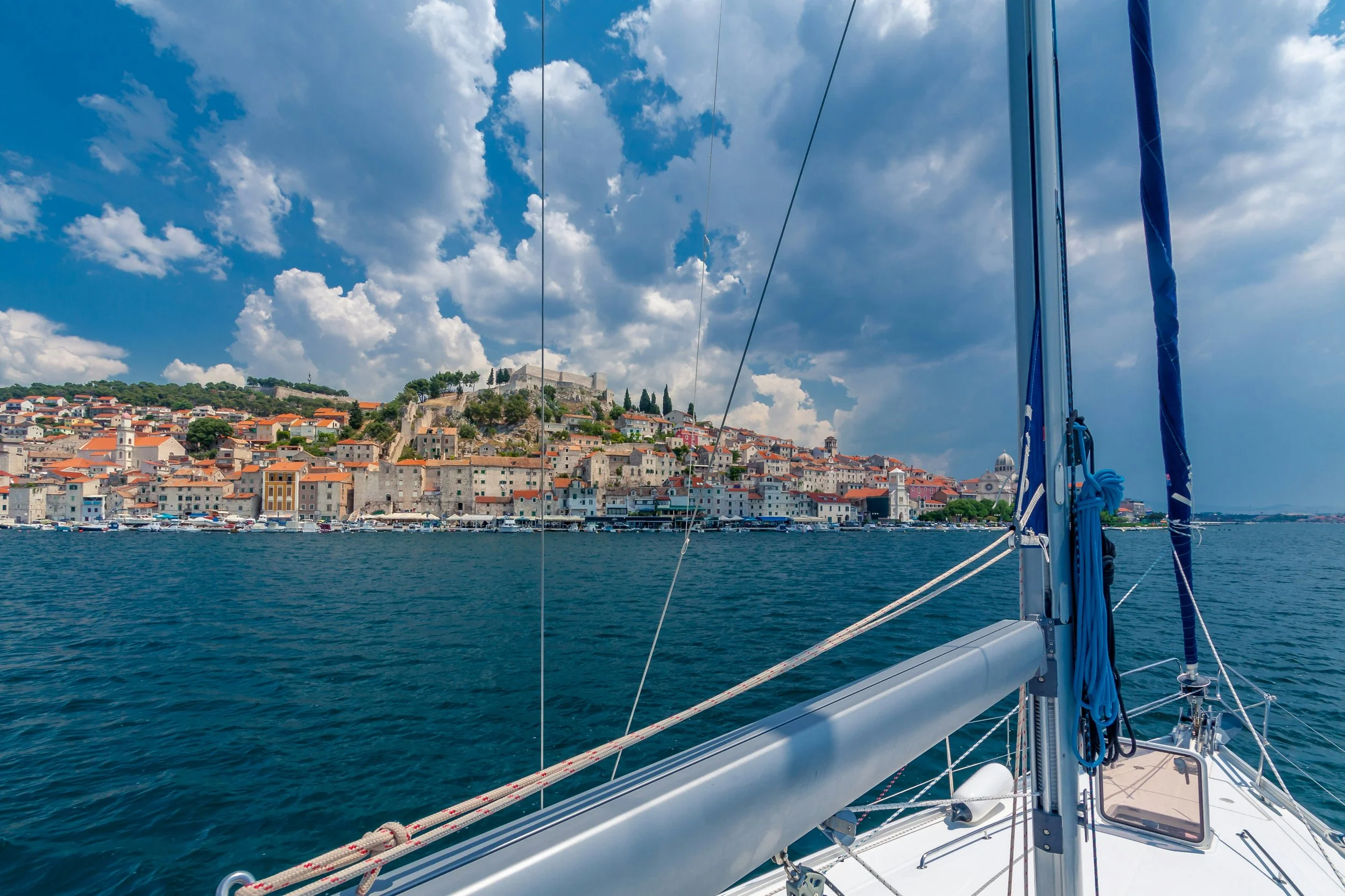 Šibenik, Croatia, viewed from a sailboat on the Adriatic Sea, with the historic coastal town and surrounding islands in the distance.