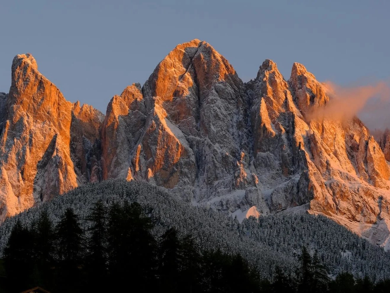 Enrosadira in the Dolomites, Italy, featuring mountain peaks glowing in shades of pink, red, and orange at sunrise or sunset.