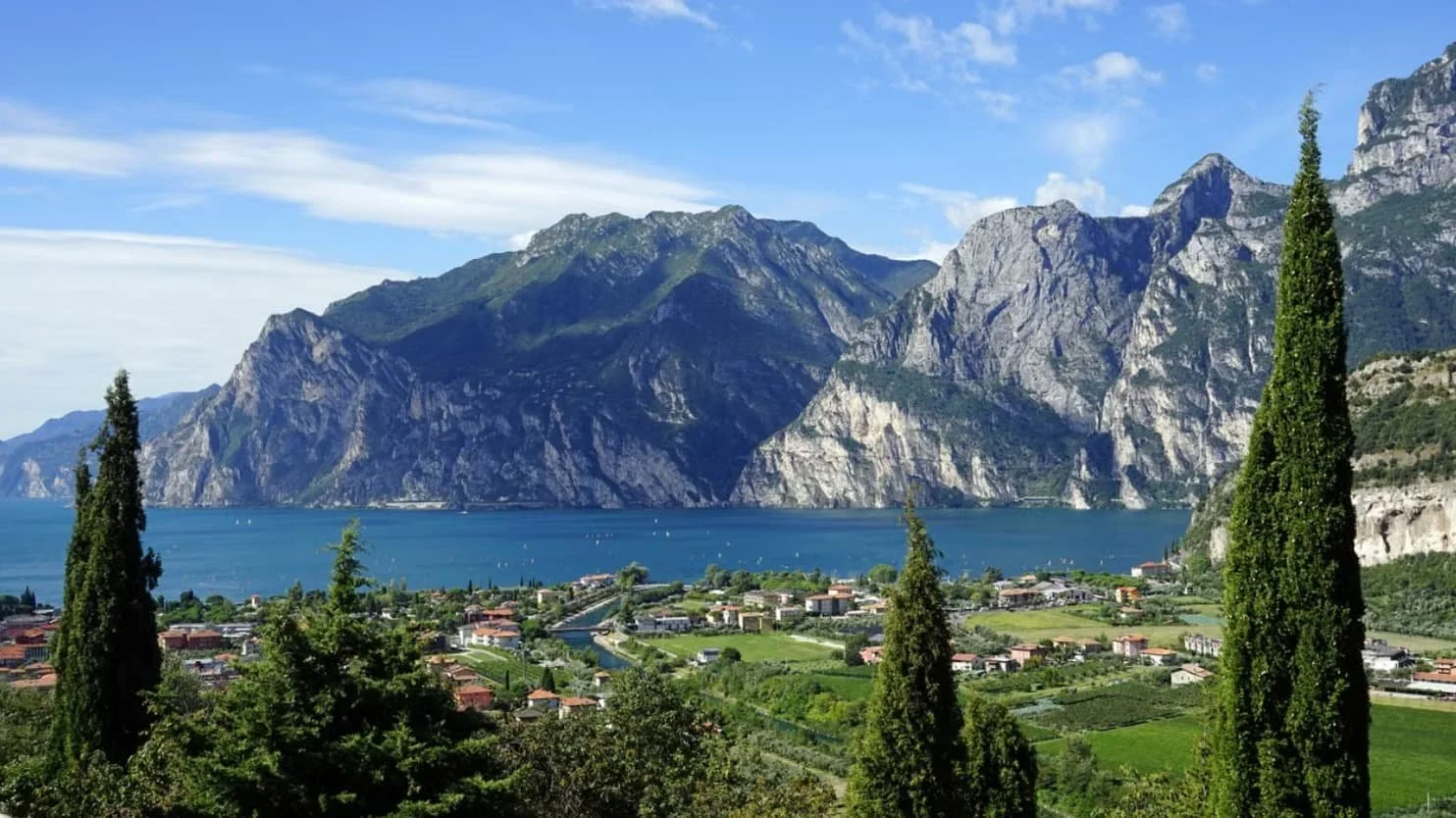 Lake Garda, northern Italy, featuring sparkling blue waters surrounded by lush green mountains and tree-lined shores.