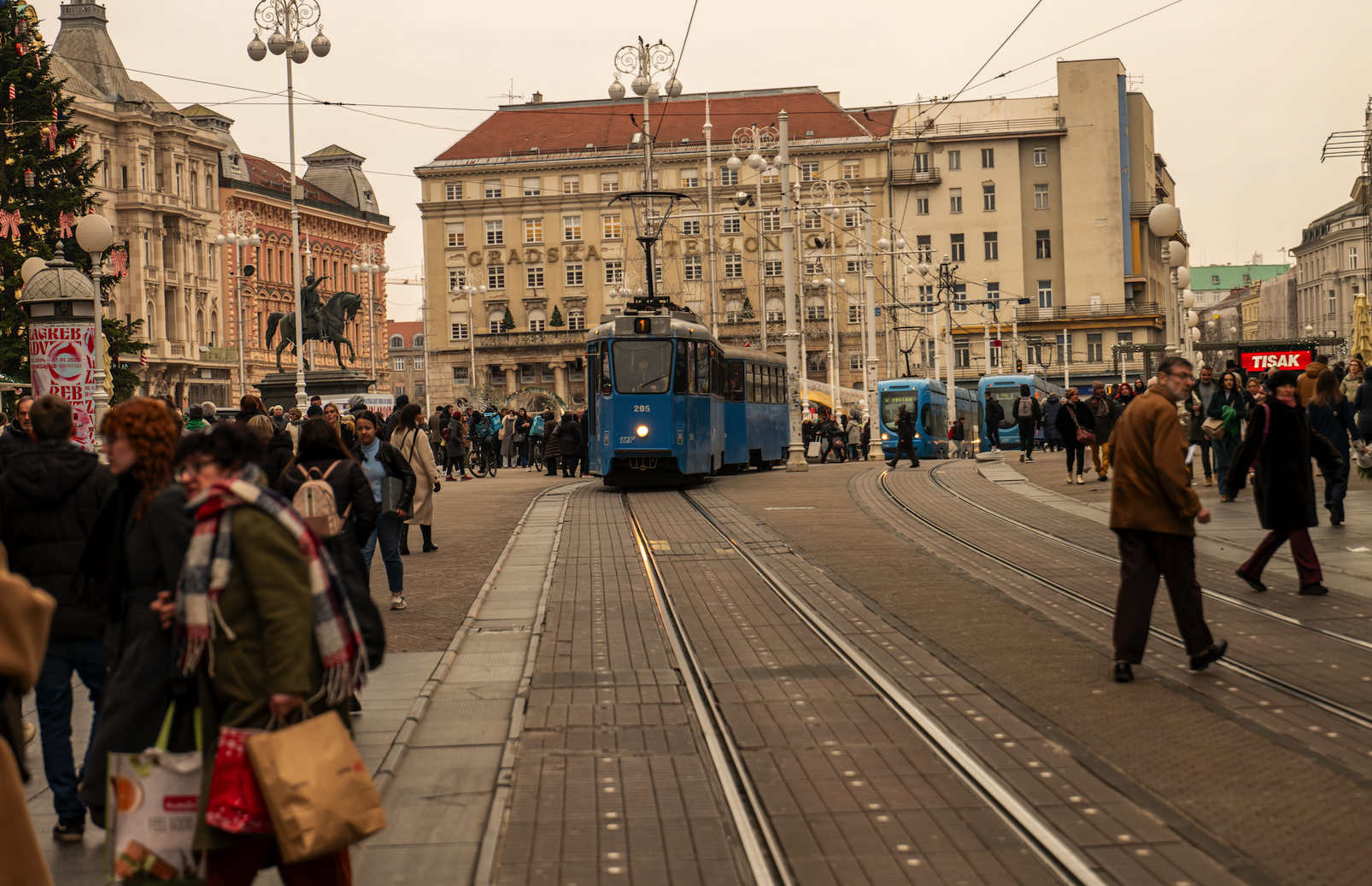 Zagreb, Croatia, featuring a blue tram and pedestrians crossing a busy city street.
