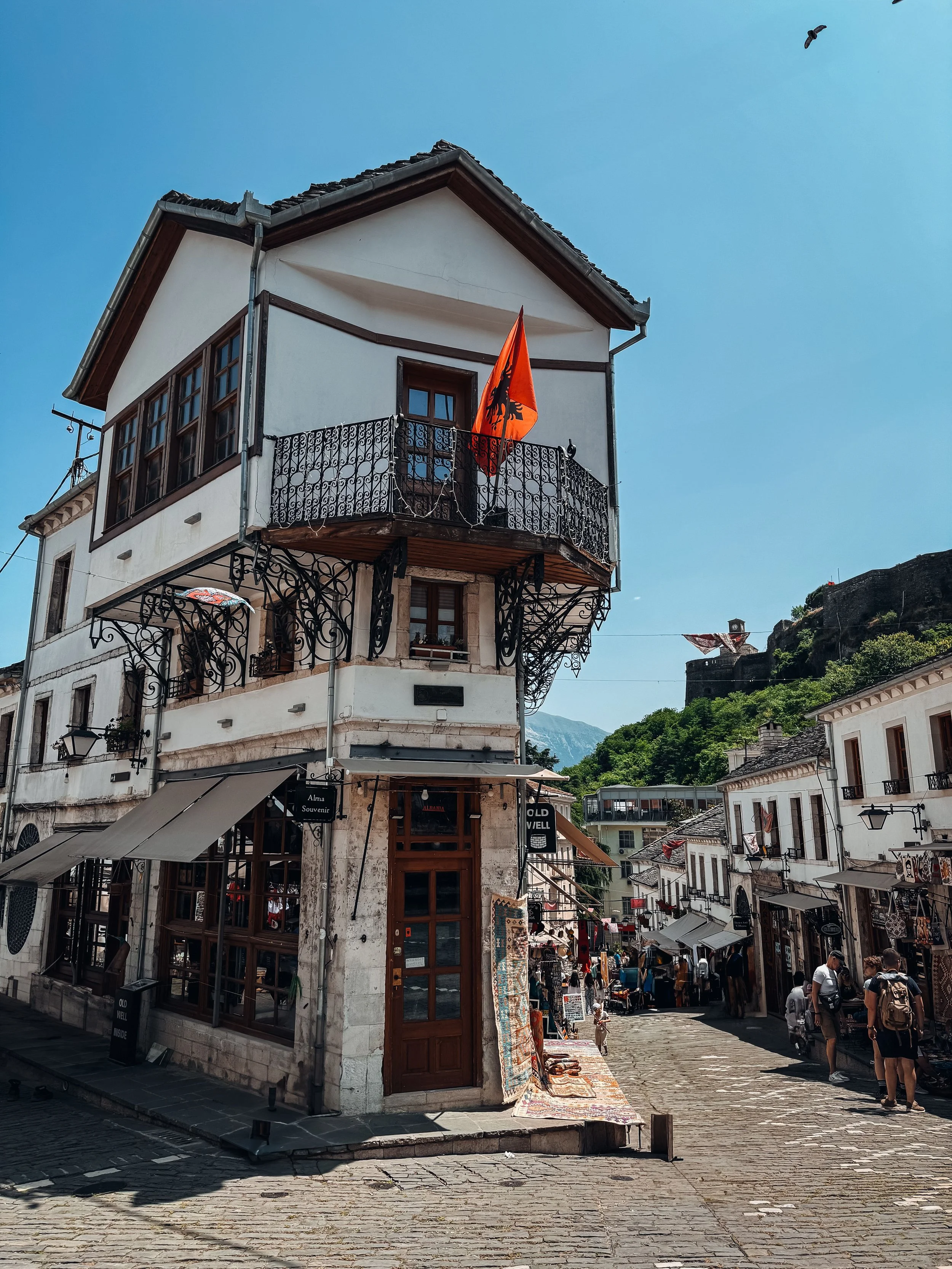 Gjirokastër, Albania, featuring a charming historic street lined with traditional stone architecture and the Albanian flag.