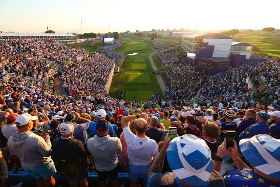 Large gallery of spectators lining the fairways and grandstands at a Ryder Cup golf event.