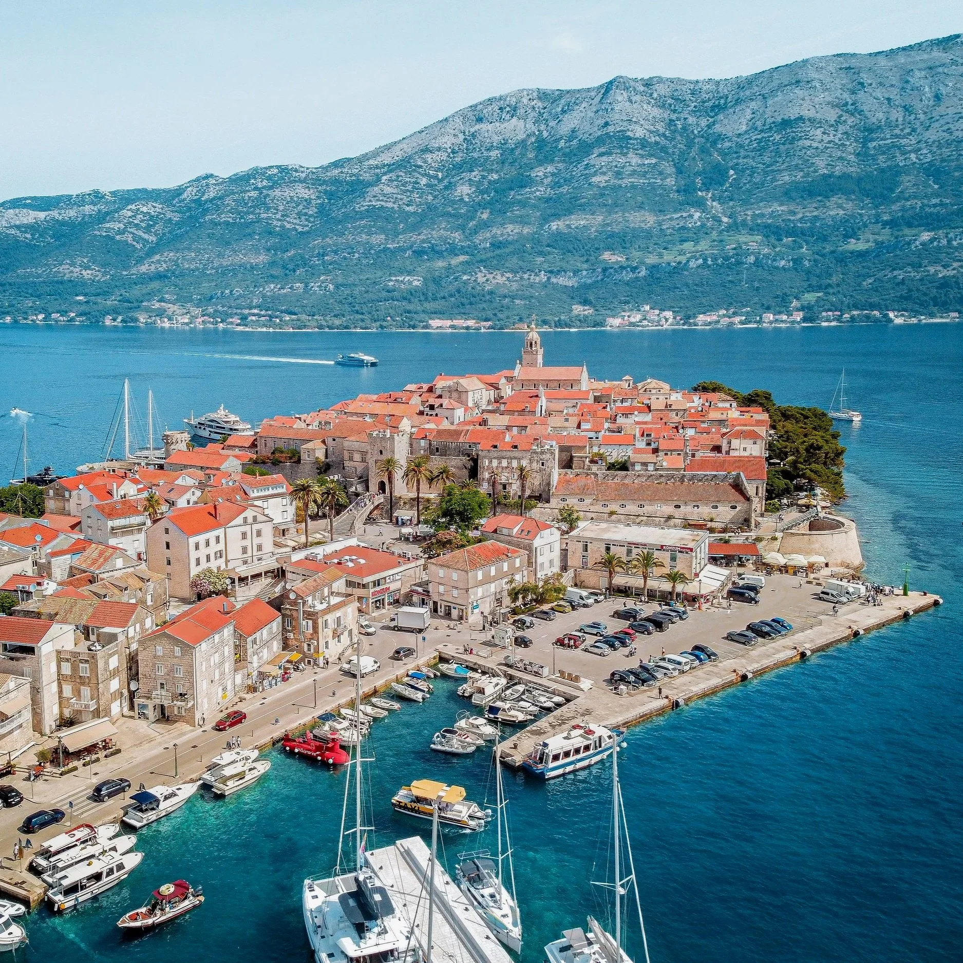 Korčula Old Town and its marina, Croatia, featuring historic stone buildings and red-tiled rooftops along the Adriatic Sea.