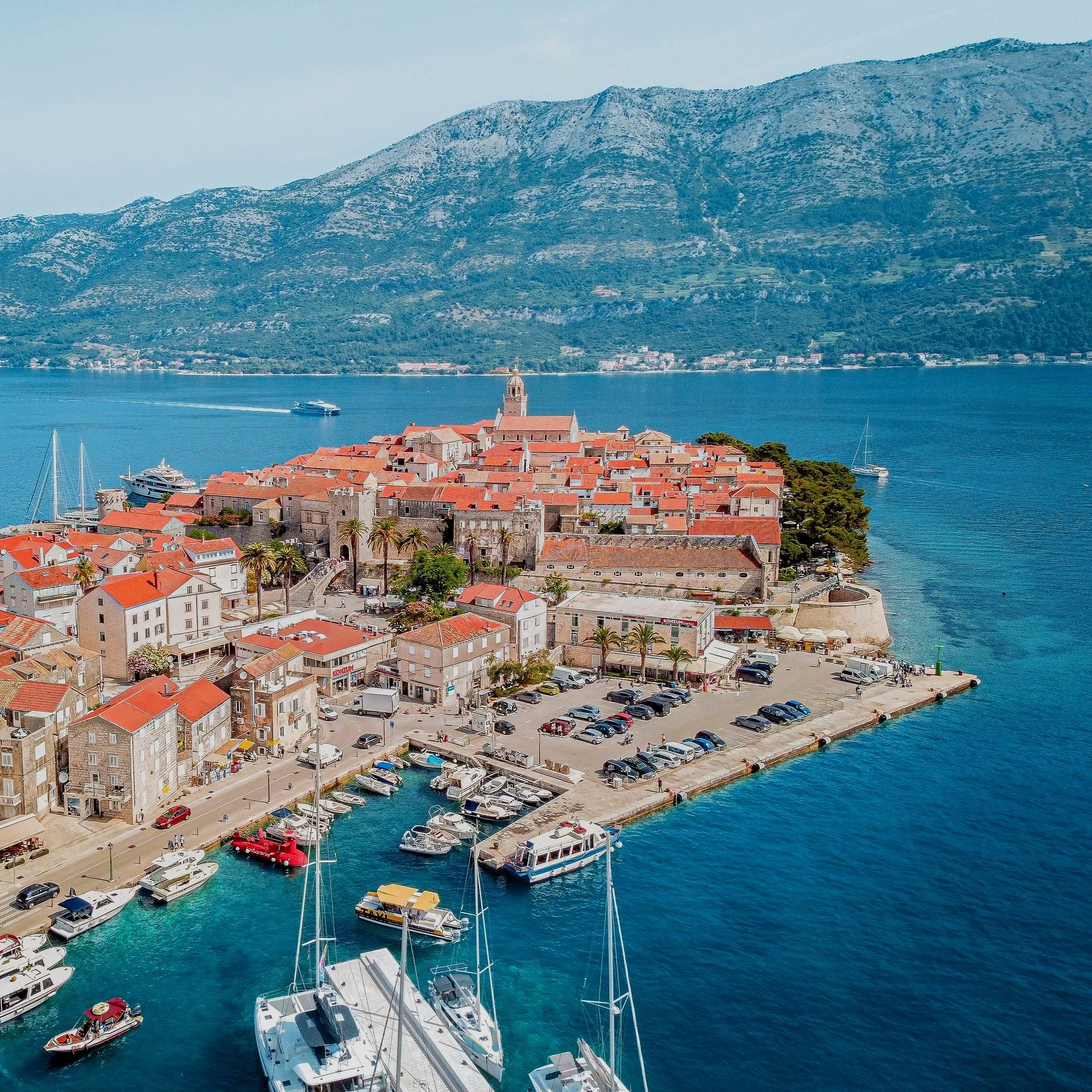 Korčula Old Town and its marina, Croatia, featuring historic stone buildings and red-tiled rooftops along the Adriatic Sea.