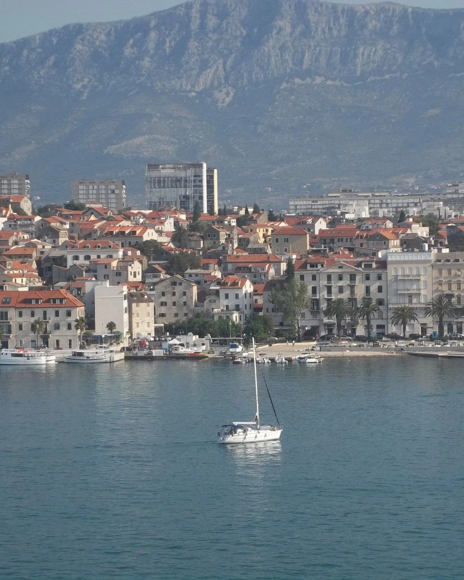 Split, Croatia, featuring a scenic coastline with a sailboat, sparkling Adriatic waters, and mountain views.
