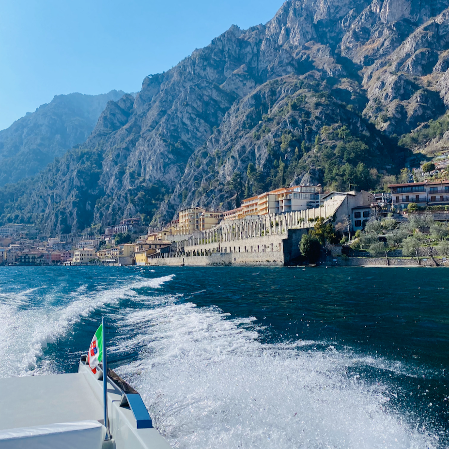 Speedboat creating water wake on Lake Garda with view of Limone sul Garda town and mountains in Italy