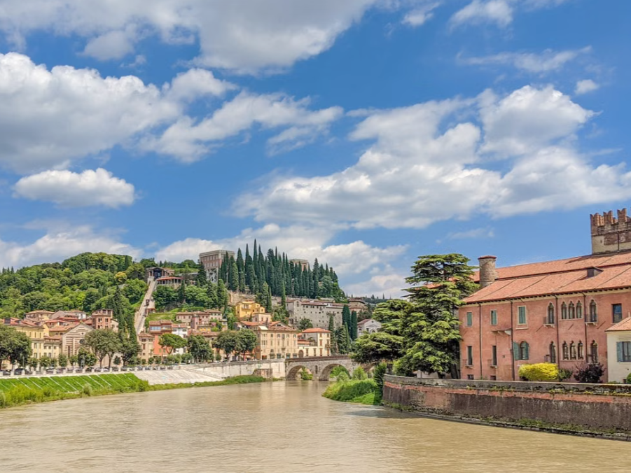 Verona, Italy, featuring the Adige River winding past historic architecture and lush green hills.