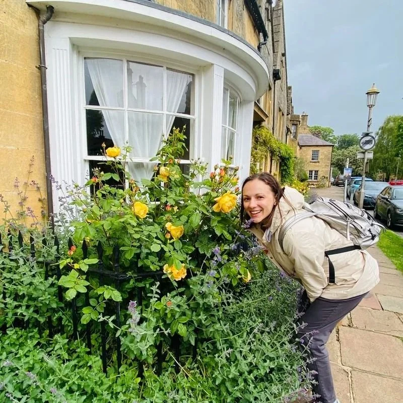 Charming Cotswold street with a historic storefront and vibrant yellow roses in England.
