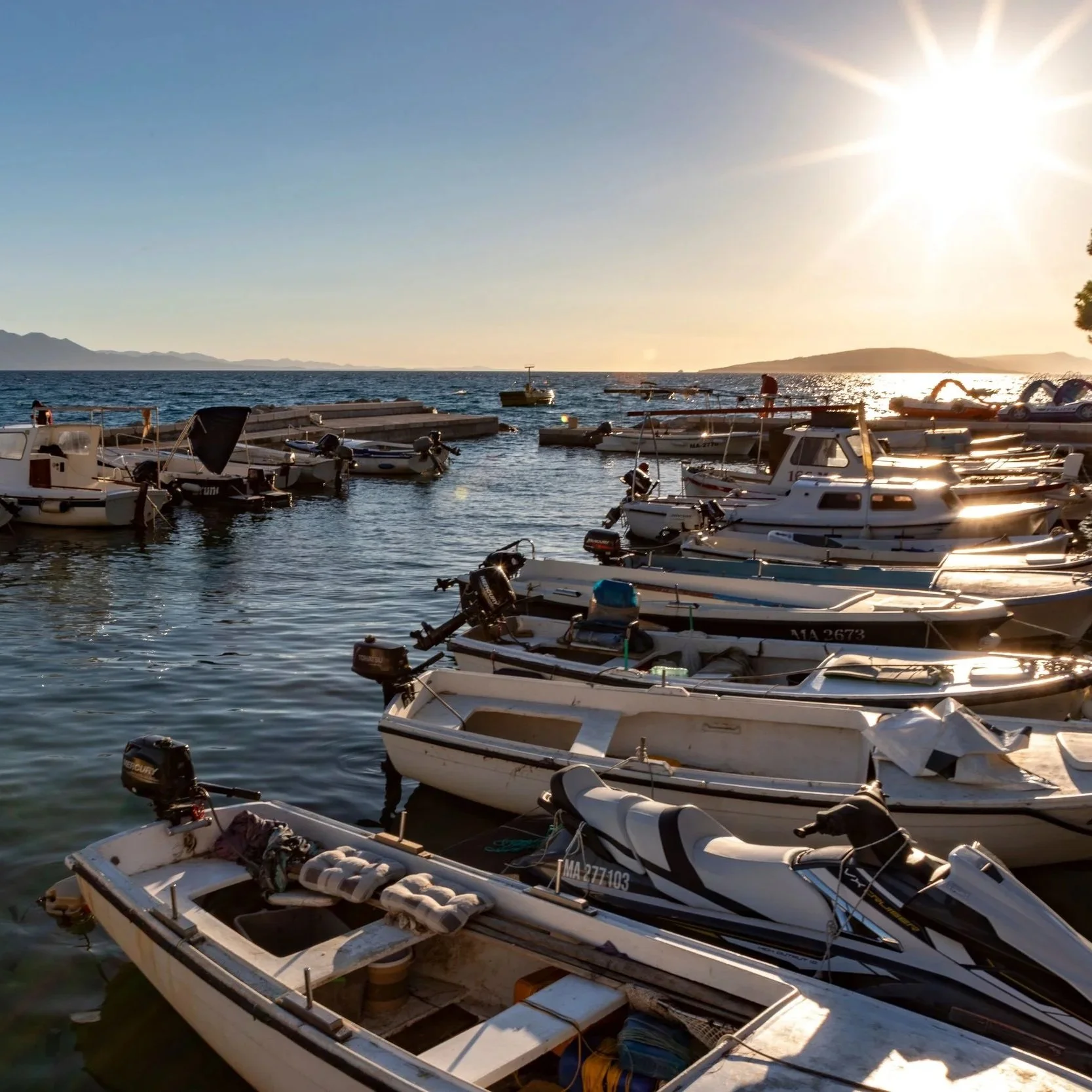 Zaostrog Harbour, Croatia, with boats illuminated by the warm light of sunset over the Adriatic Sea.