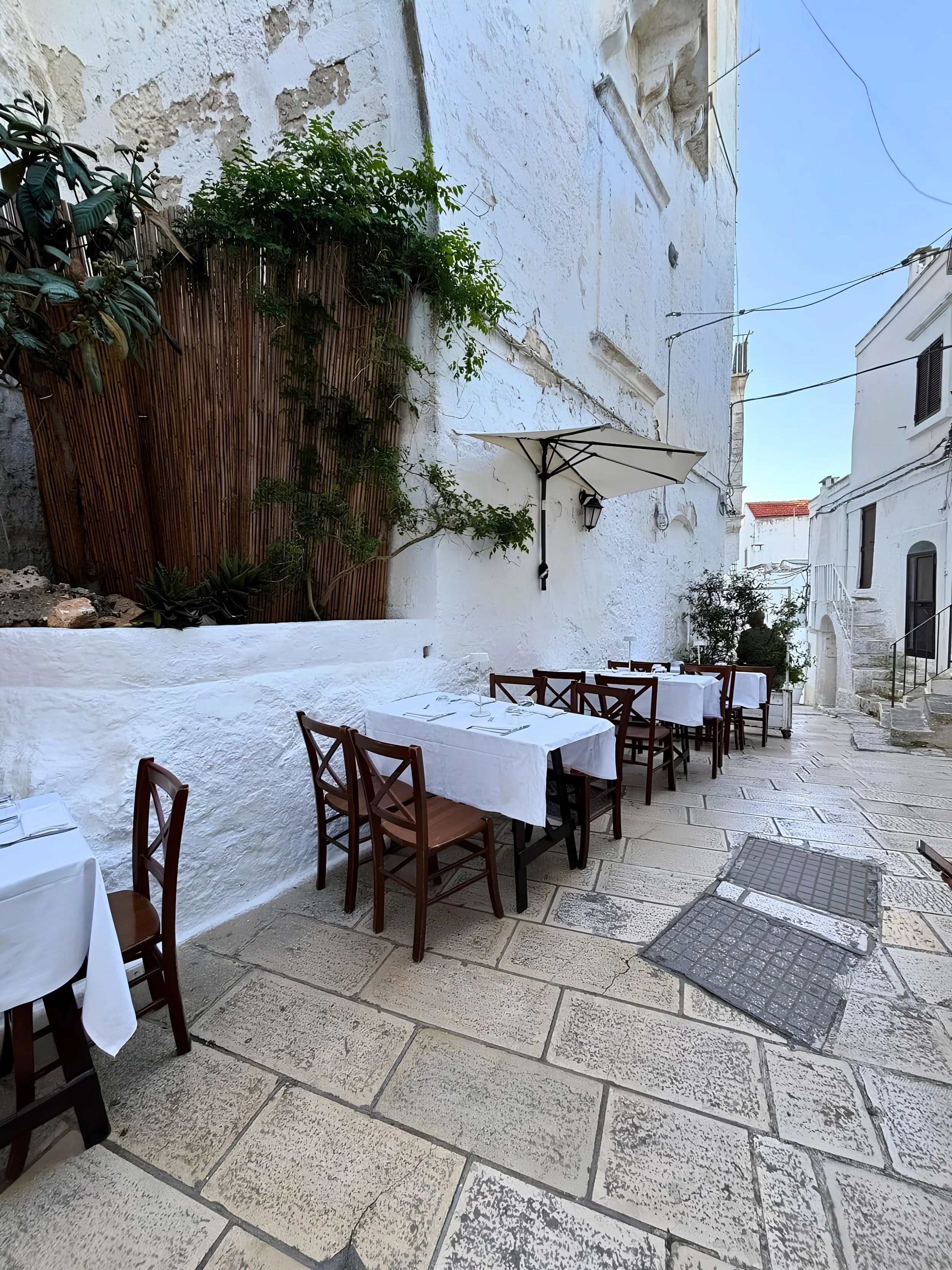 Narrow whitewashed alley lined with charming stone buildings and outdoor dining areas in Ostuni, Puglia, Italy.