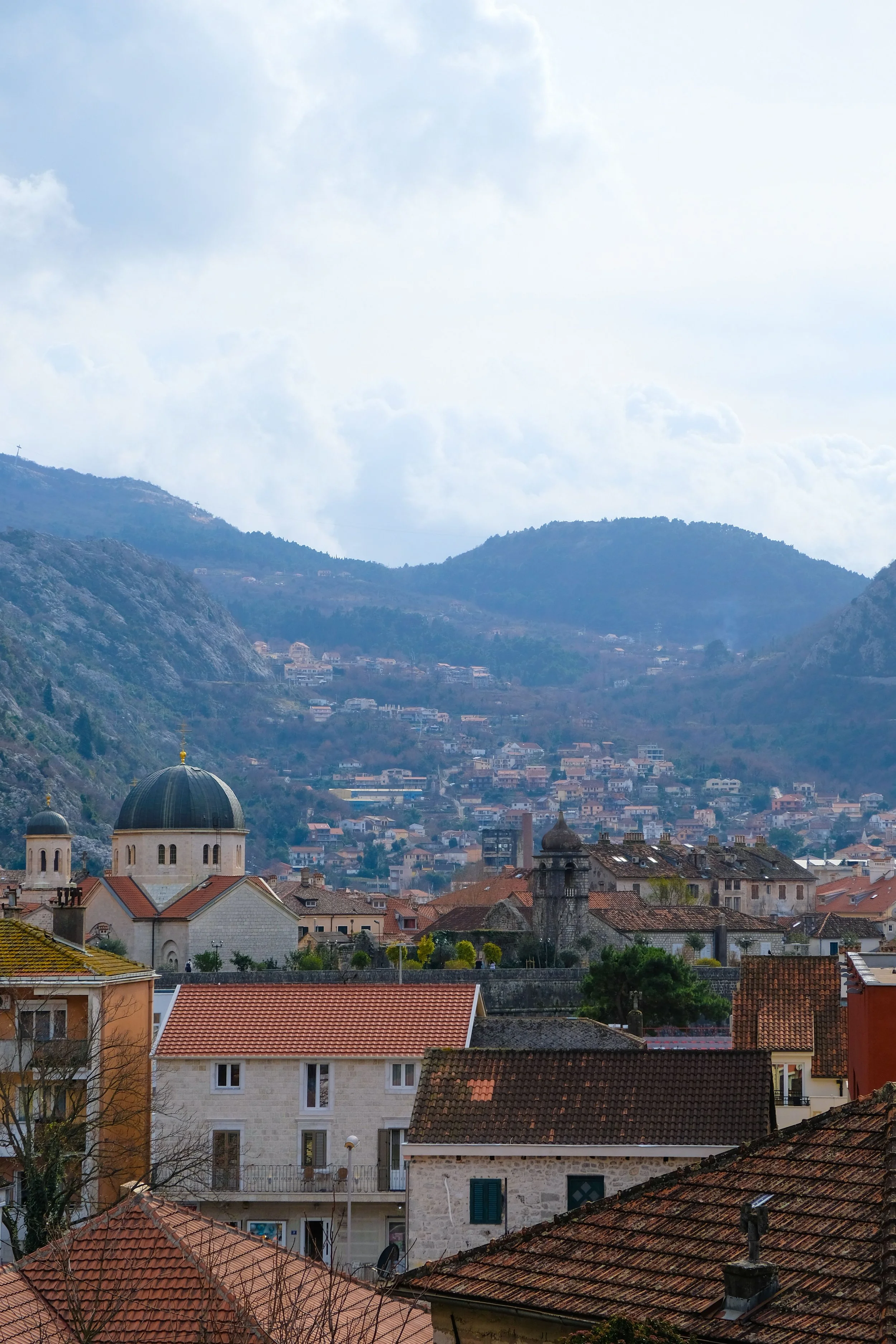 Kotor, Montenegro, featuring traditional rooftops, historic stone buildings, and a dramatic mountainous backdrop.