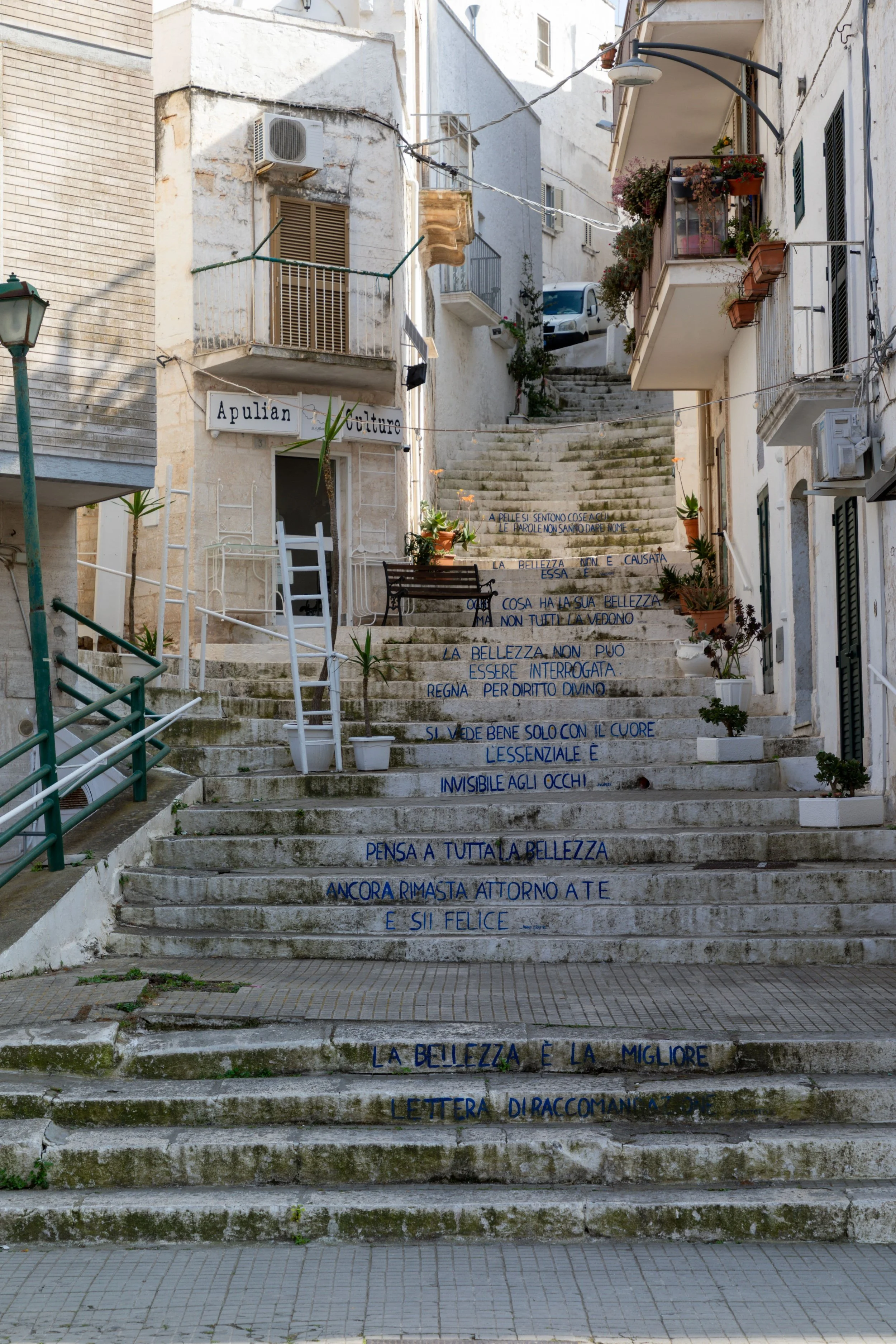 Whitewashed alley with stone steps decorated with Italian poetry in Ostuni, Puglia, Italy.