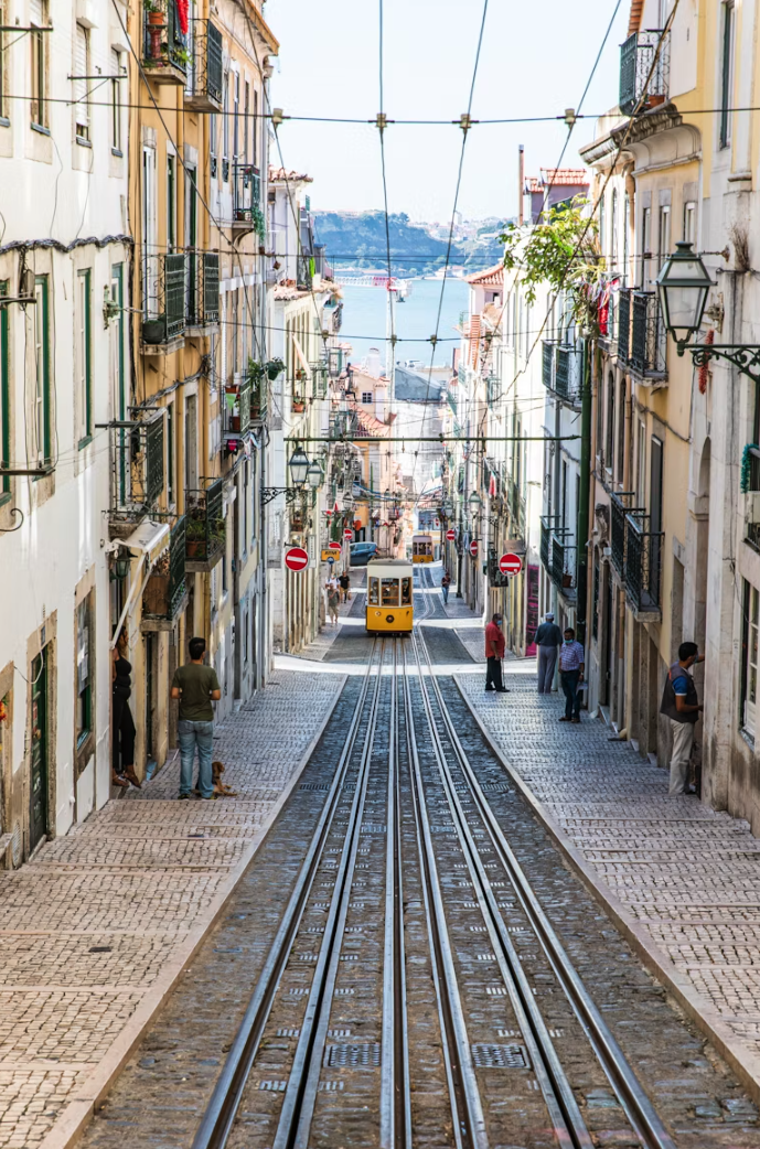 Bica Funicular descending Rua da Bica de Duarte Belo in Lisbon, Portugal, with the Tagus River in the background.
