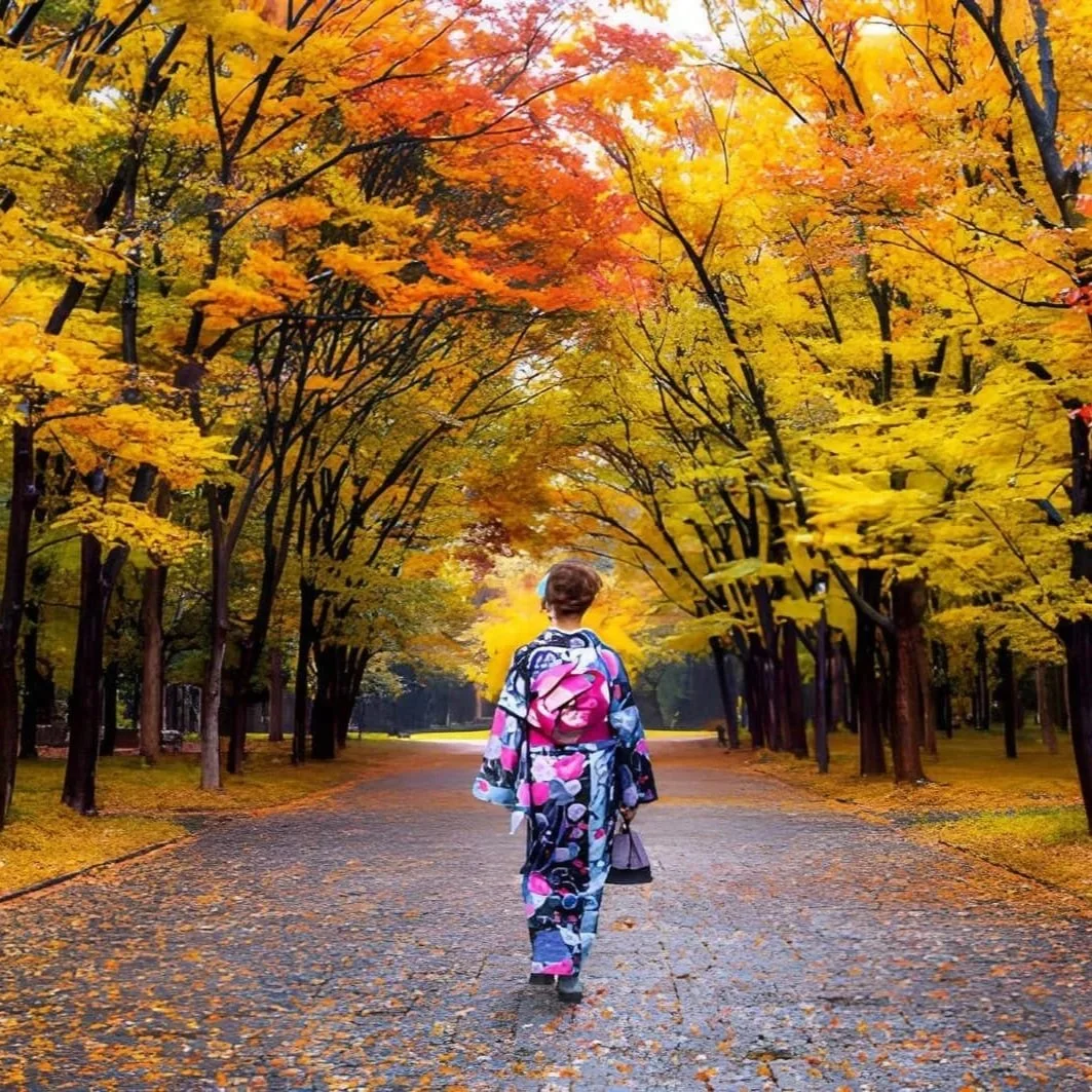 Woman in a floral patterned kimono walking down a tree-lined path surrounded by golden autumn leaves.