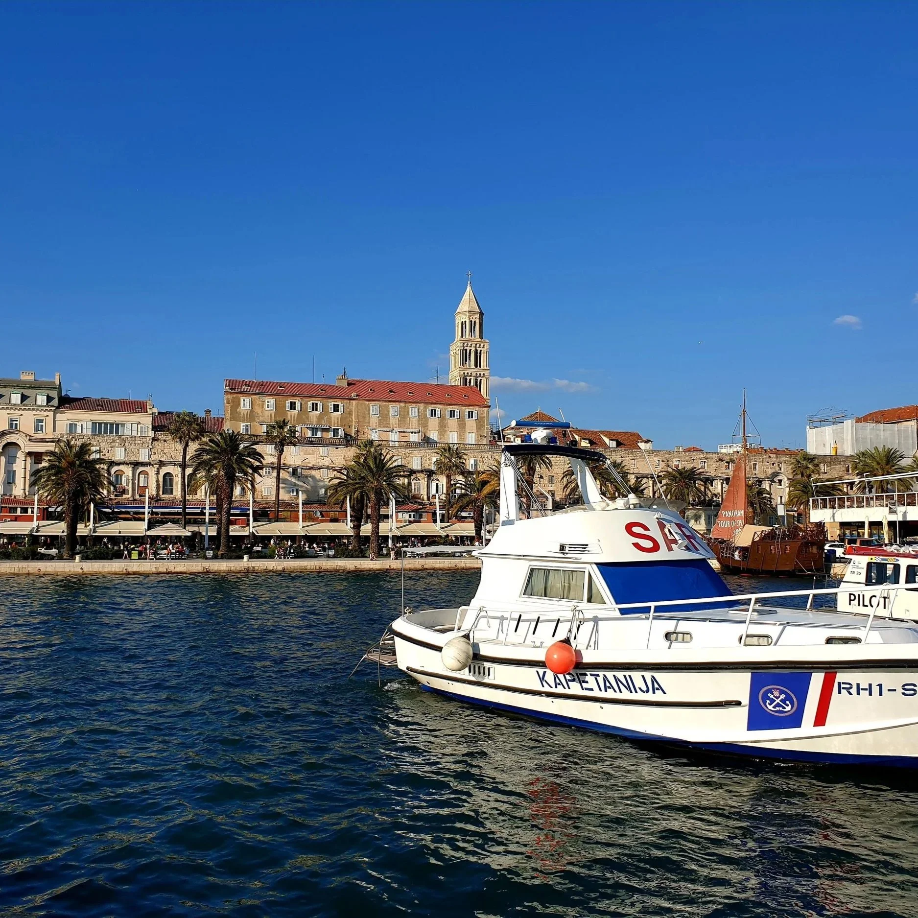 Split Harbour, Croatia, featuring boats, palm trees, and the Adriatic coast beneath a clear blue sky.