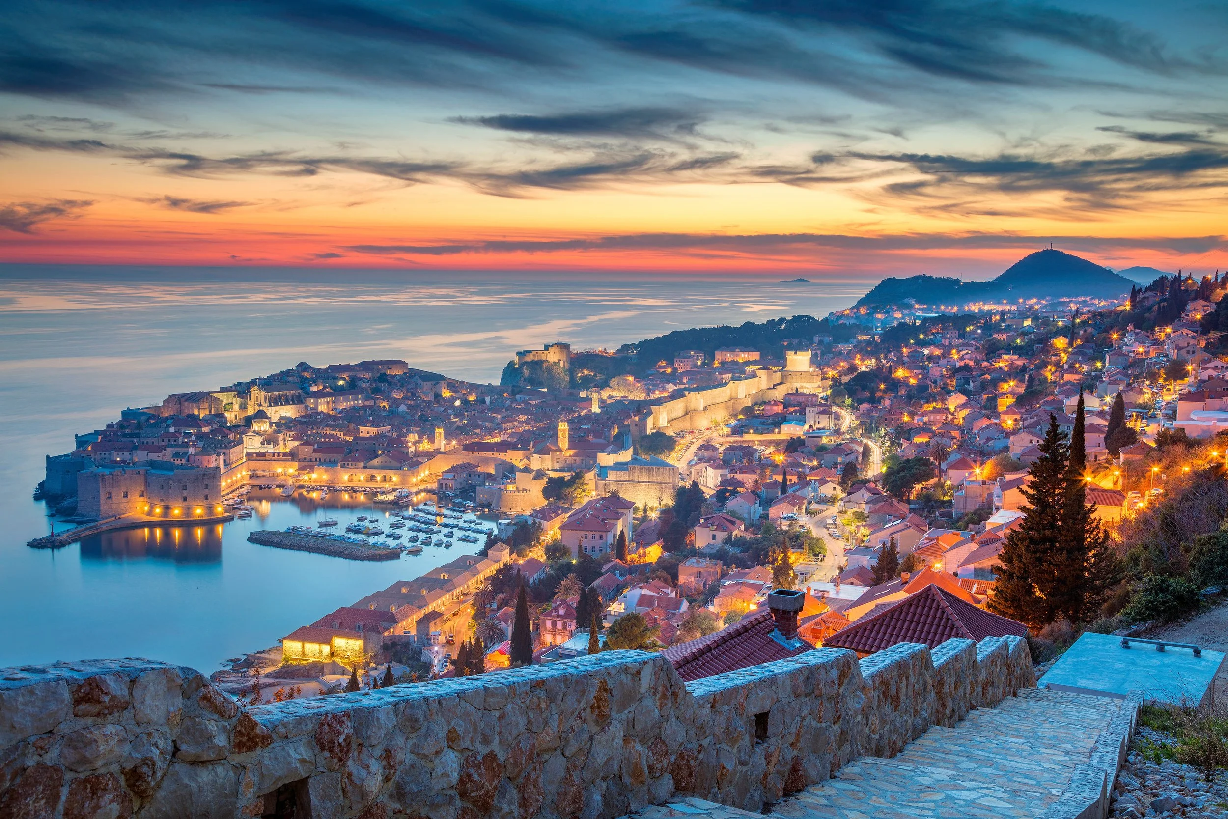Dubrovnik, Croatia, at sunset, with historic stone walls, terracotta rooftops, and the Adriatic Sea surrounding the Old Town.