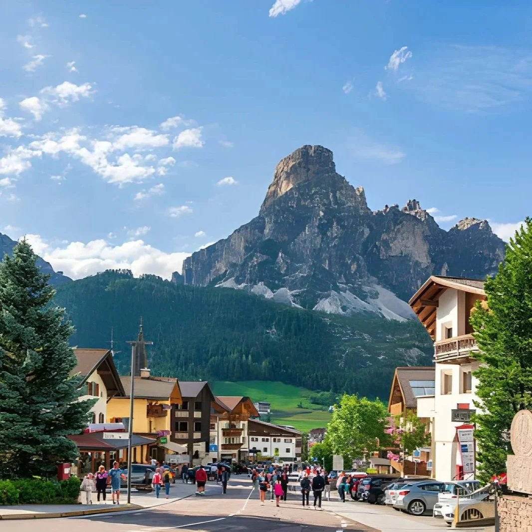 Picturesque Alpine village street in Corvara, Alta Badia with traditional chalets, tourists, and the dramatic peak of Sassongher mountain in the Italian Dolomites.