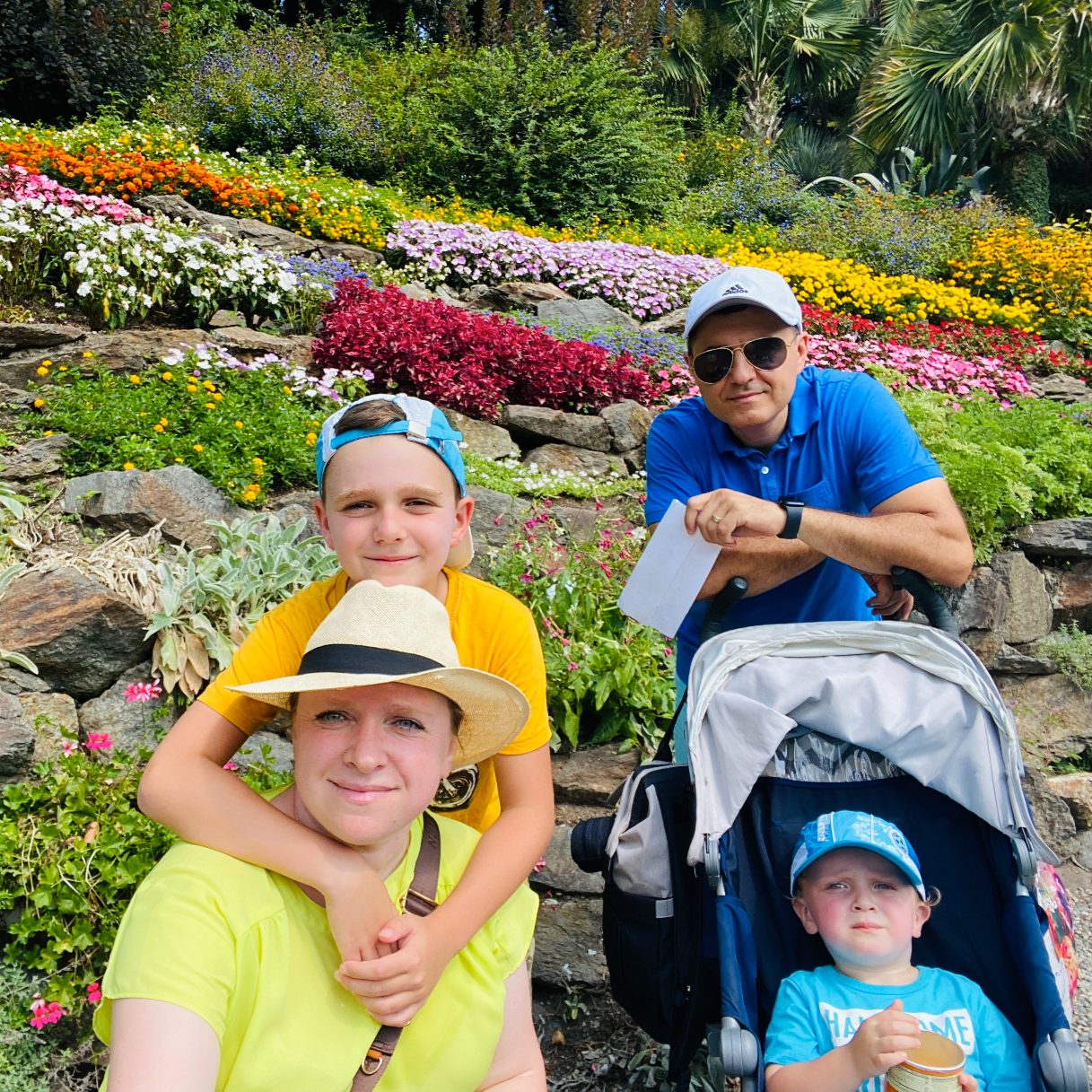 Happy family of four posing outdoors together during a summer vacation in front of a colorful, blooming terraced flower garden.