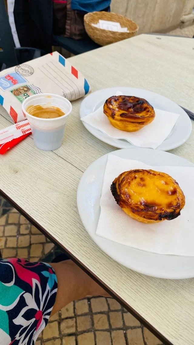 A Portuguese pastel de nata on a white plate, featuring a golden, caramelized custard filling and a crisp, flaky pastry shell.