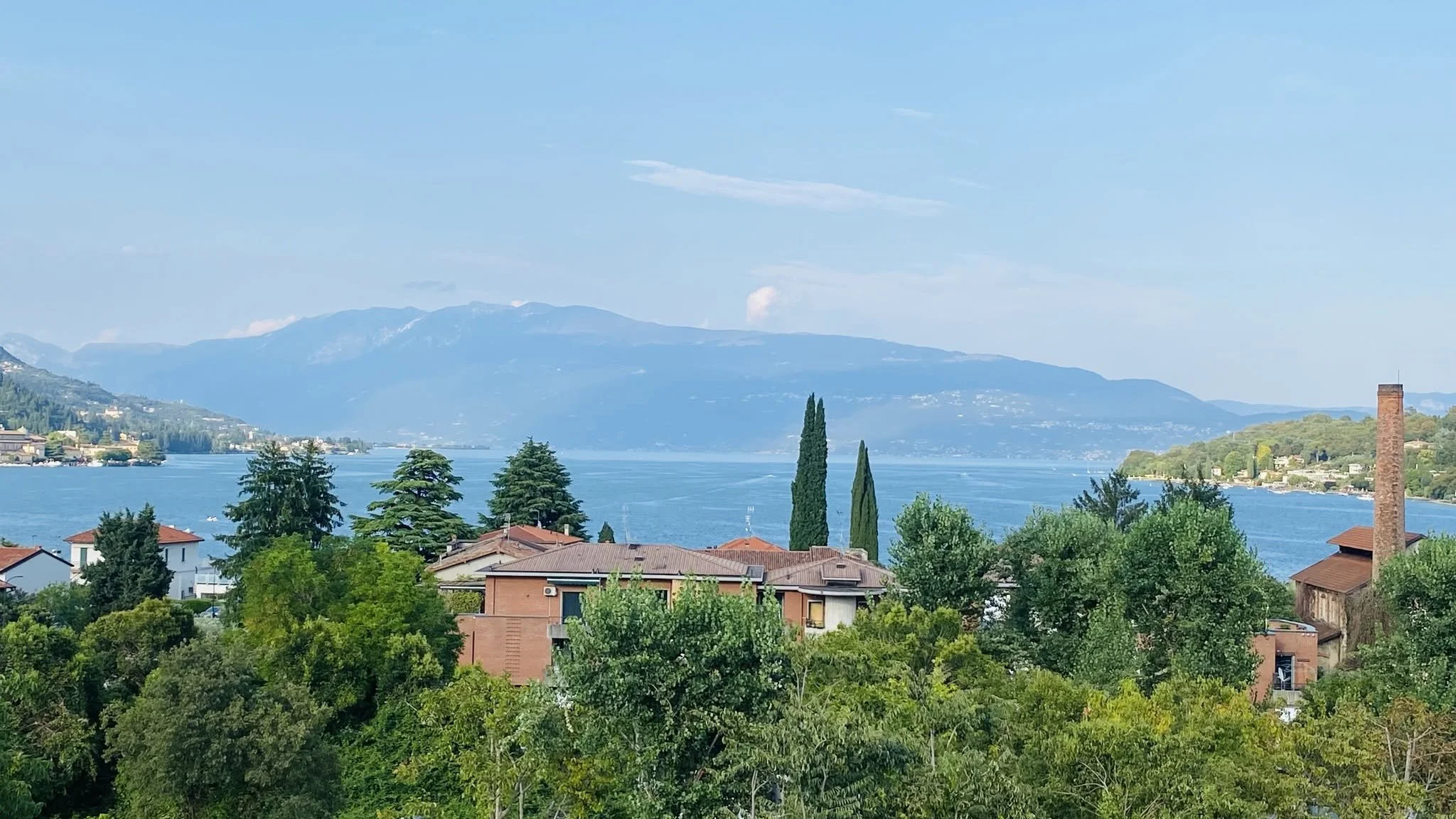 Lake Garda, northern Italy, featuring terracotta-roofed lakeside buildings, lush greenery, and surrounding mountain ranges.