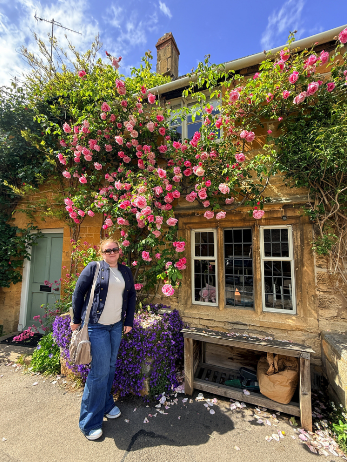 Traditional Cotswold stone cottage with climbing pink roses on High Street in Blockley, England.