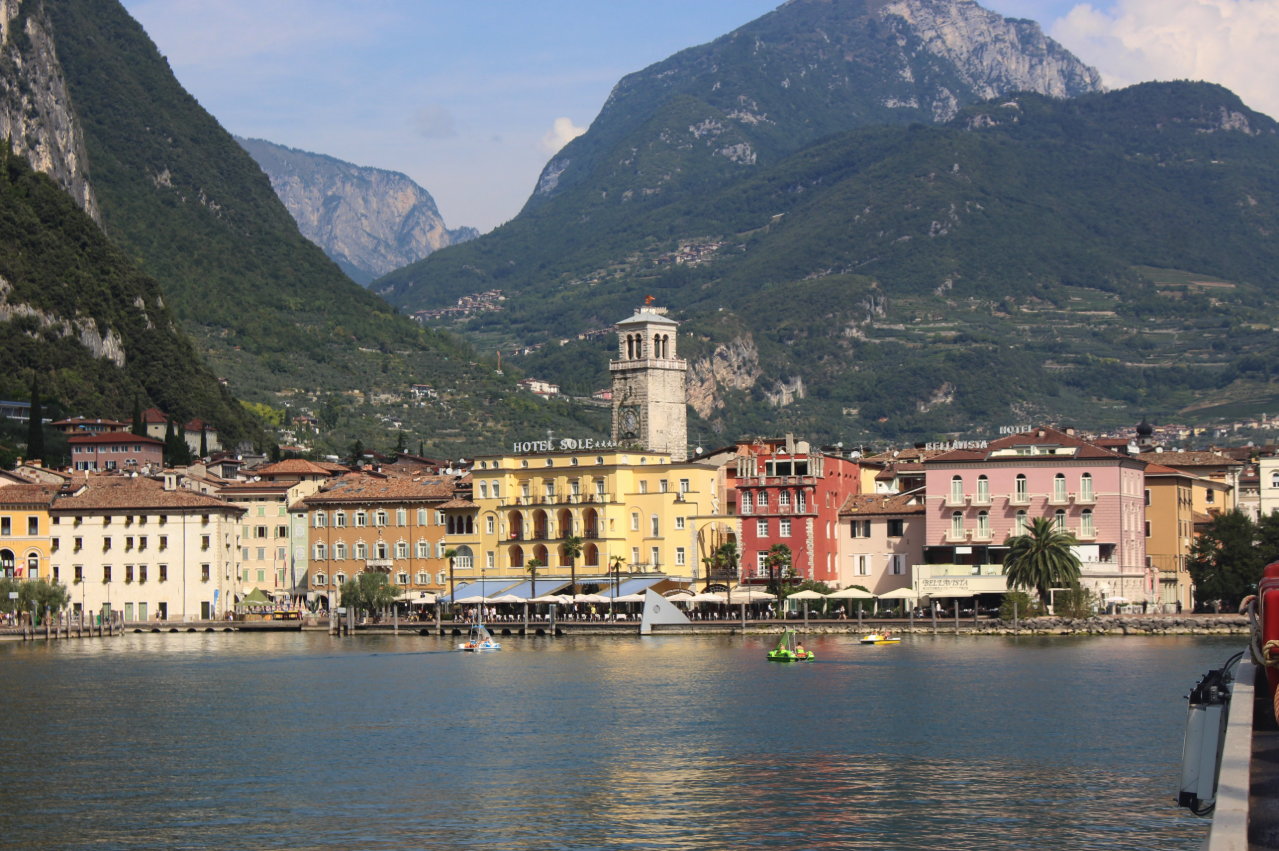 Riva del Garda, Lake Garda, Italy, featuring colorful lakeside buildings, lush green mountains, and sparkling blue water.