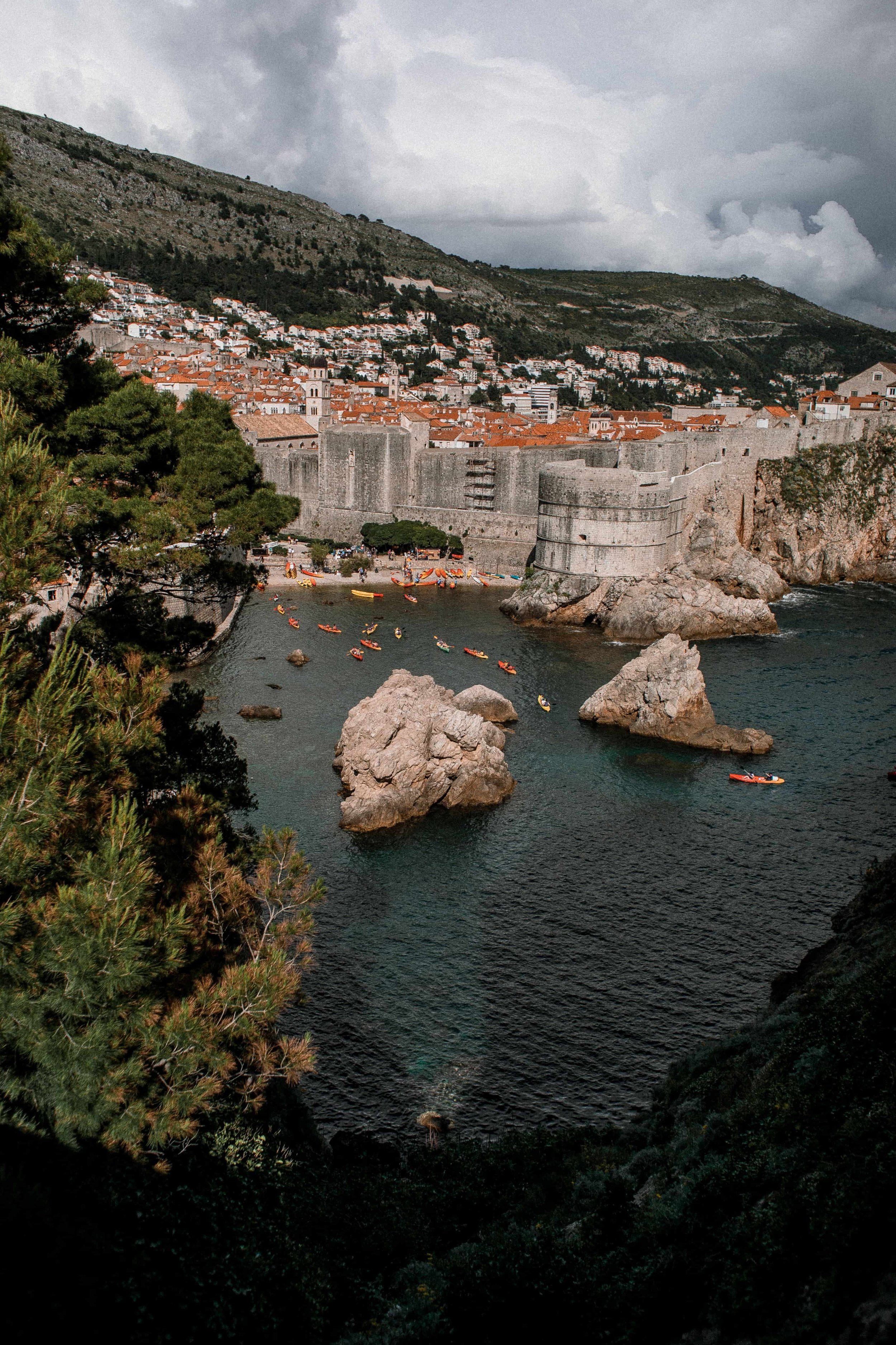 Aerial view of Dubrovnik, Croatia, featuring its historic medieval walls, lush greenery, and scenic Adriatic coastline.