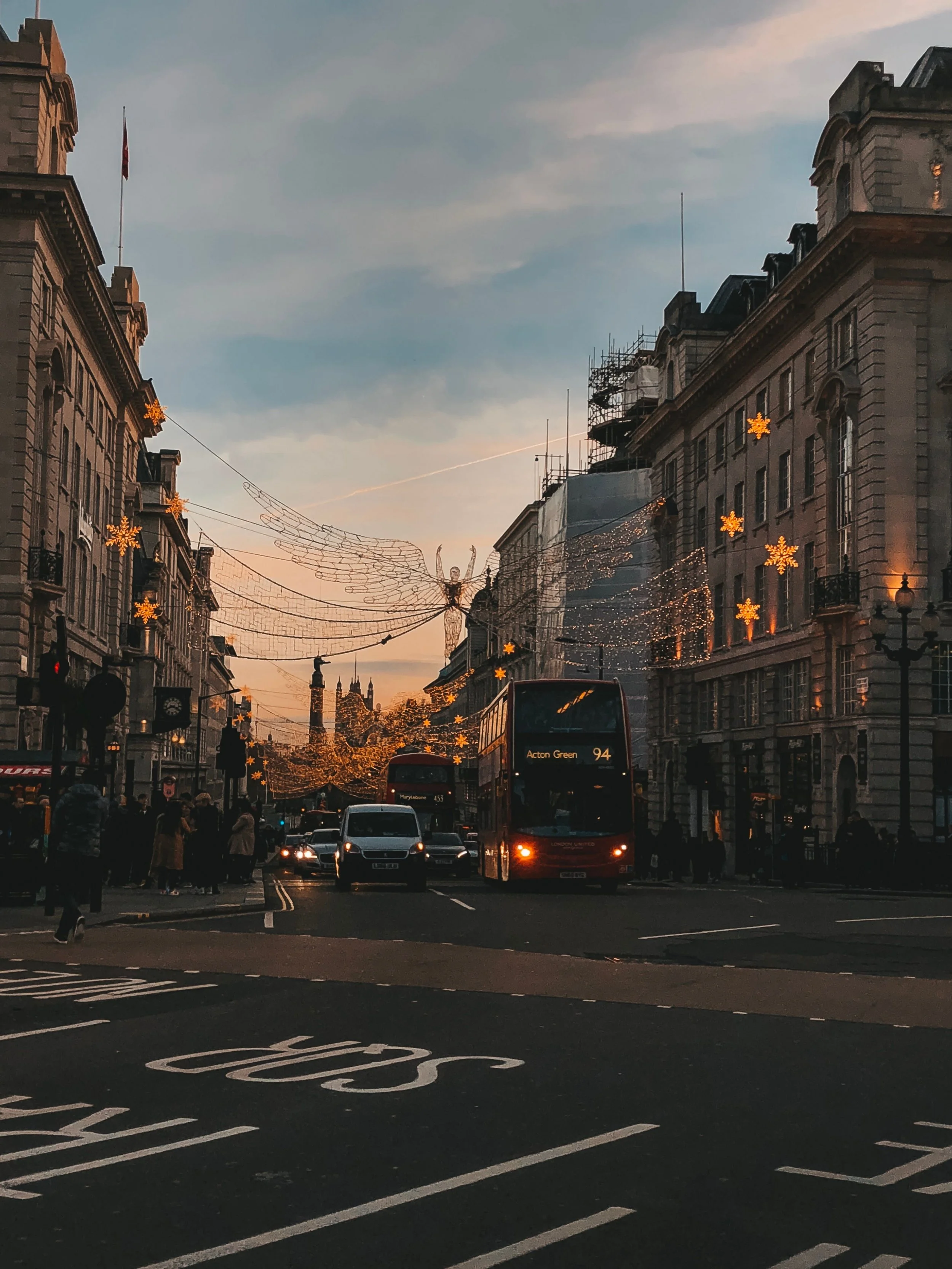 A bustling London street at twilight, illuminated by festive Christmas lights and holiday decorations.