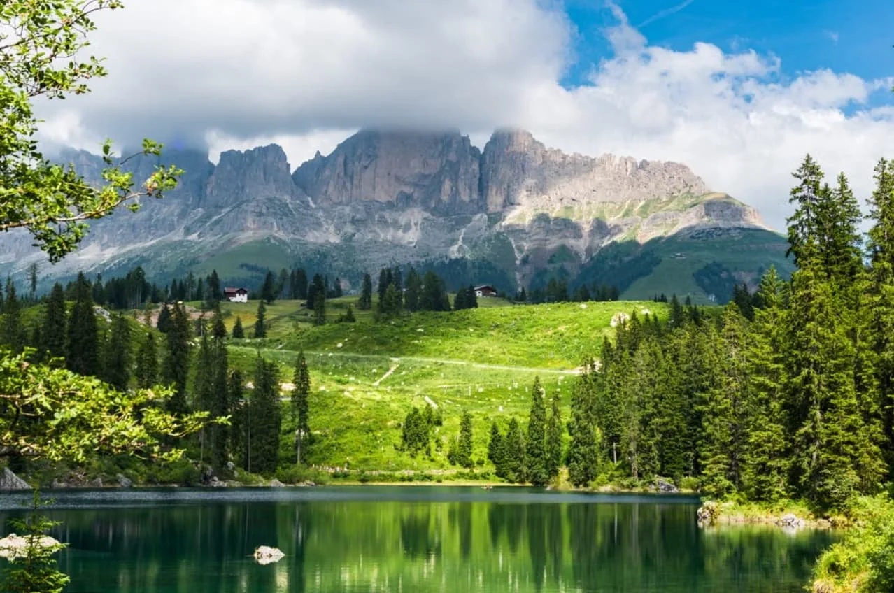 Trentino-South Tyrol, northern Italy, featuring the dramatic peaks of the Dolomites rising above lush alpine meadows and a tranquil lake.