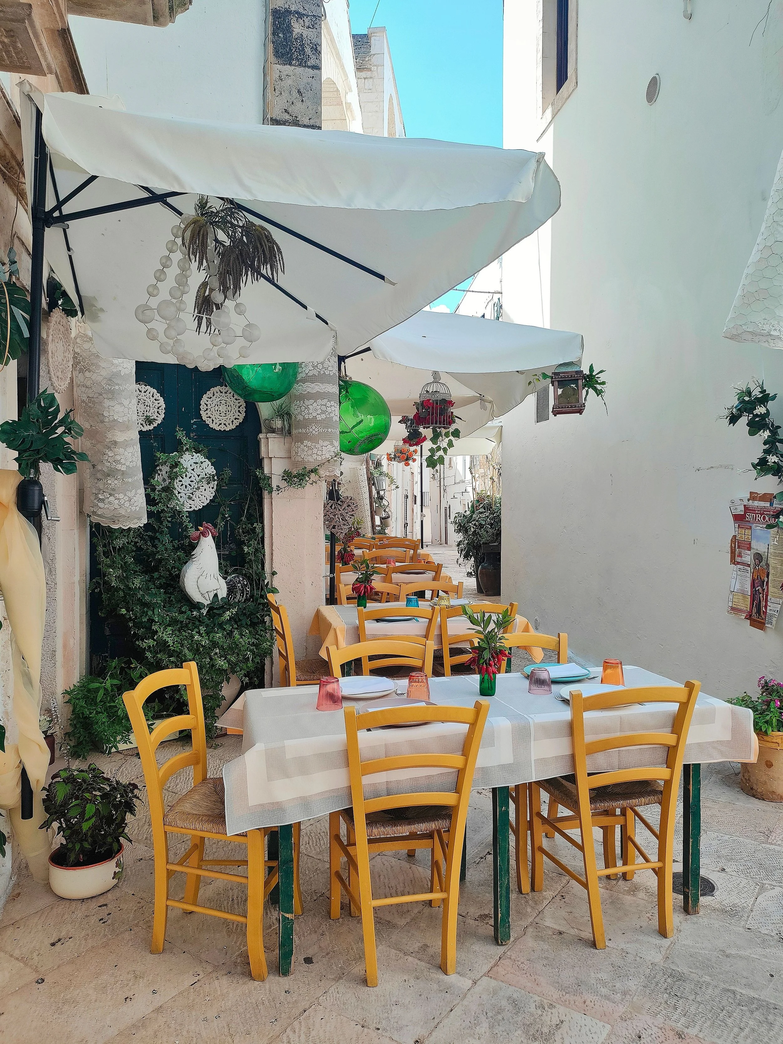 Charming outdoor dining area in a narrow whitewashed alley in Cisternino, Puglia, Italy, featuring rustic stone walls and Mediterranean decor.