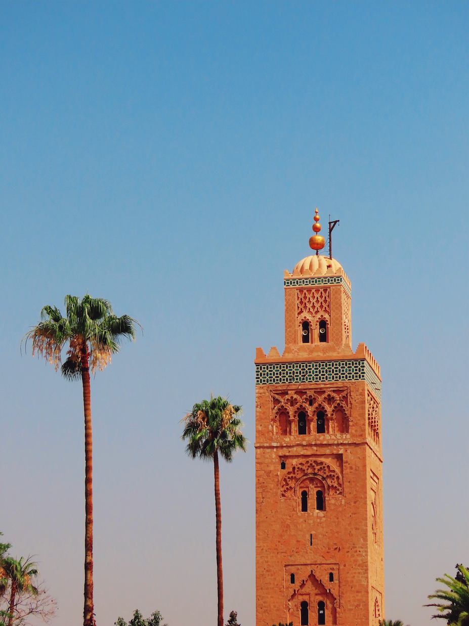 Koutoubia Mosque minaret with tall palm trees against a clear blue sky in Marrakech, Morocco