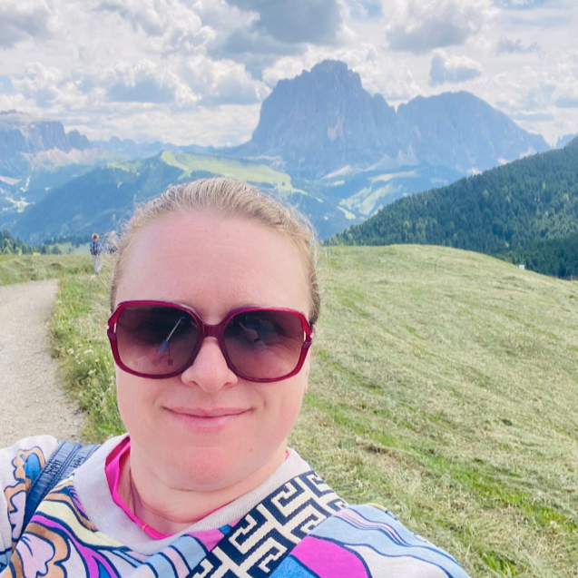 Anna Fishman, the founder of Olegana Travel Boutique taking a selfie while hiking in the Dolomites mountains, Italy, with the iconic Sassolungo peak in the background.