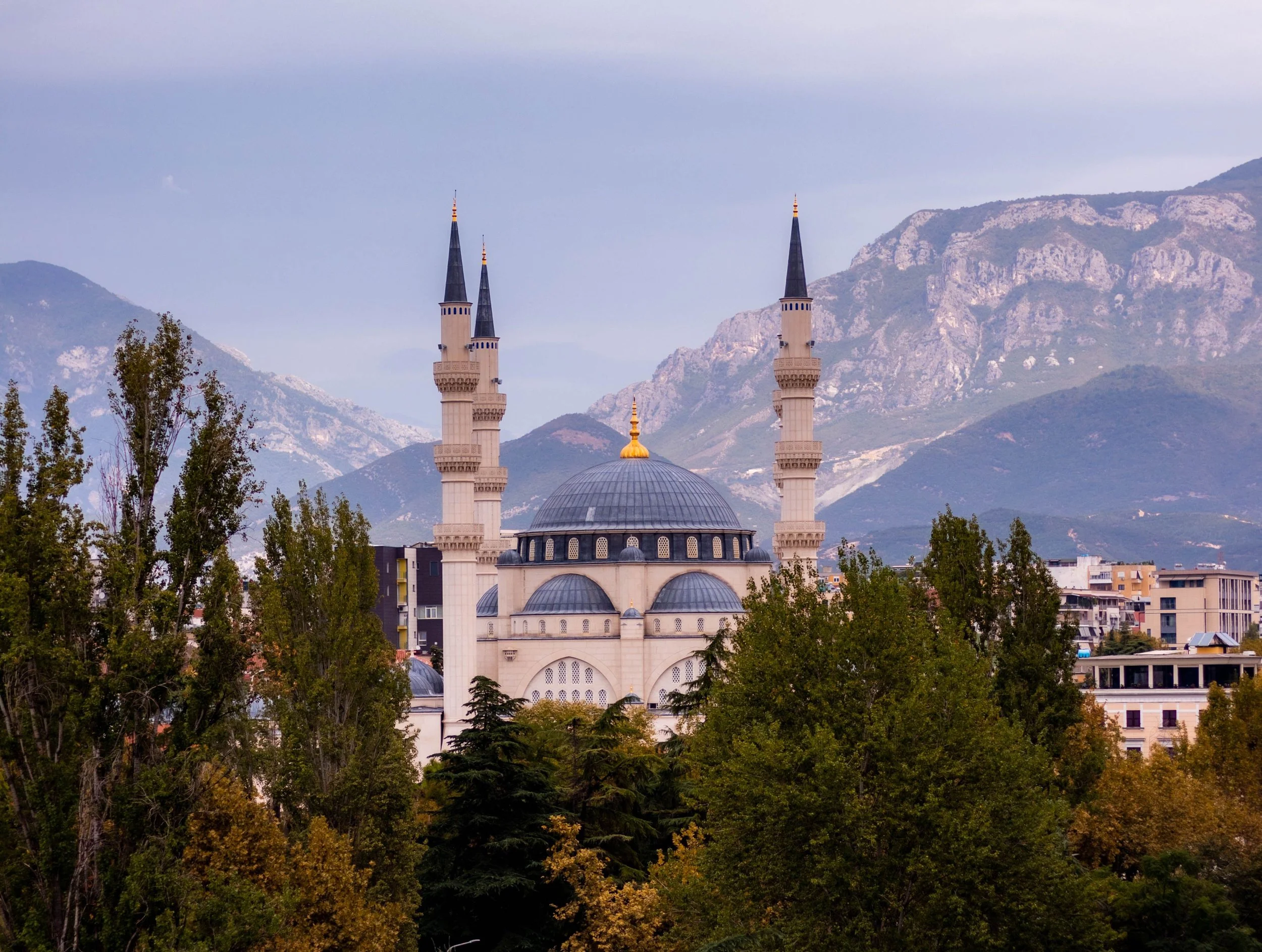 Namazgah Mosque in Tirana, Albania, featuring striking Islamic architecture framed by surrounding mountains and trees.