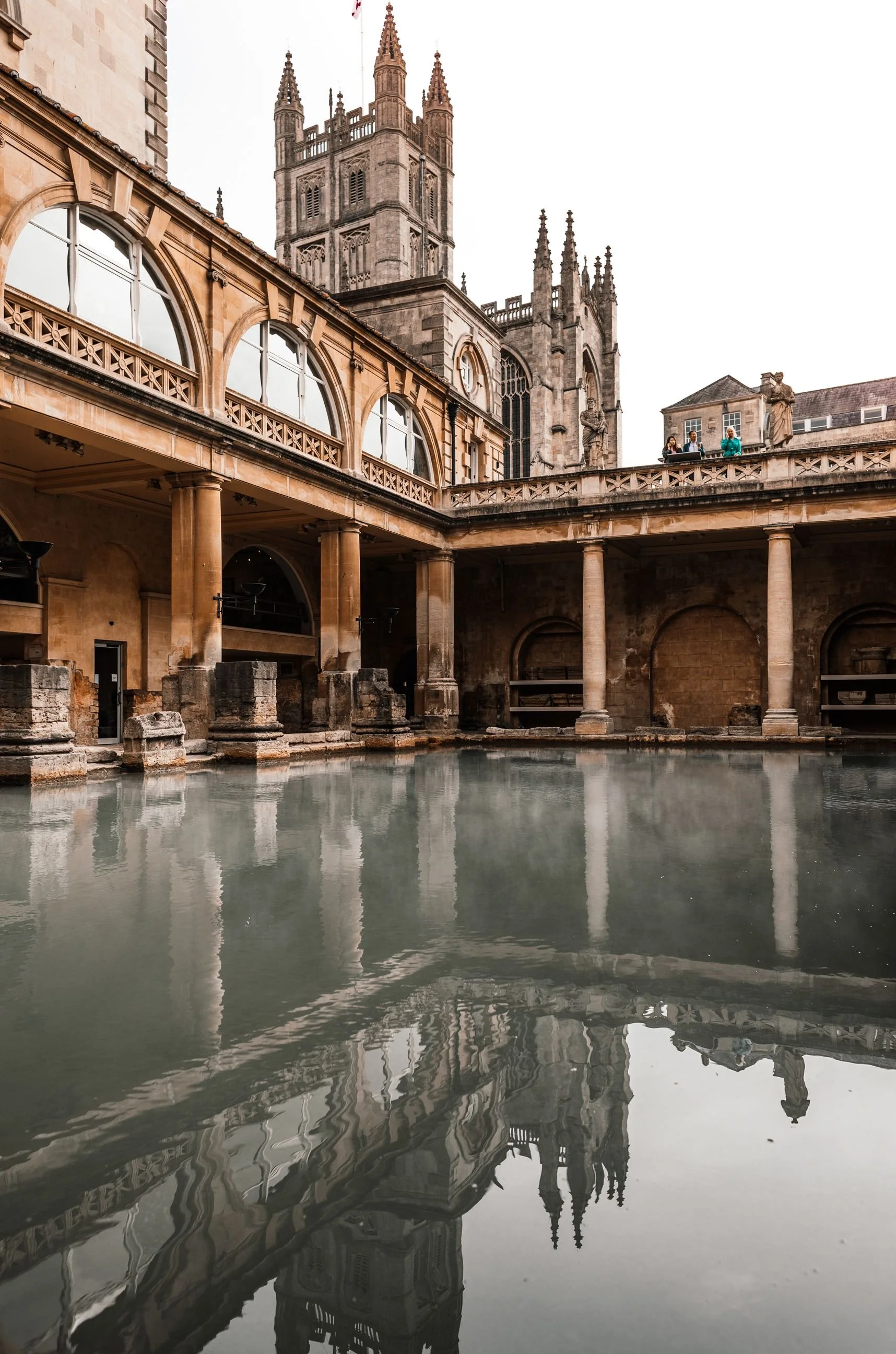 The Great Bath at the Roman Baths with steam rising and the abbey behind, Bath, England