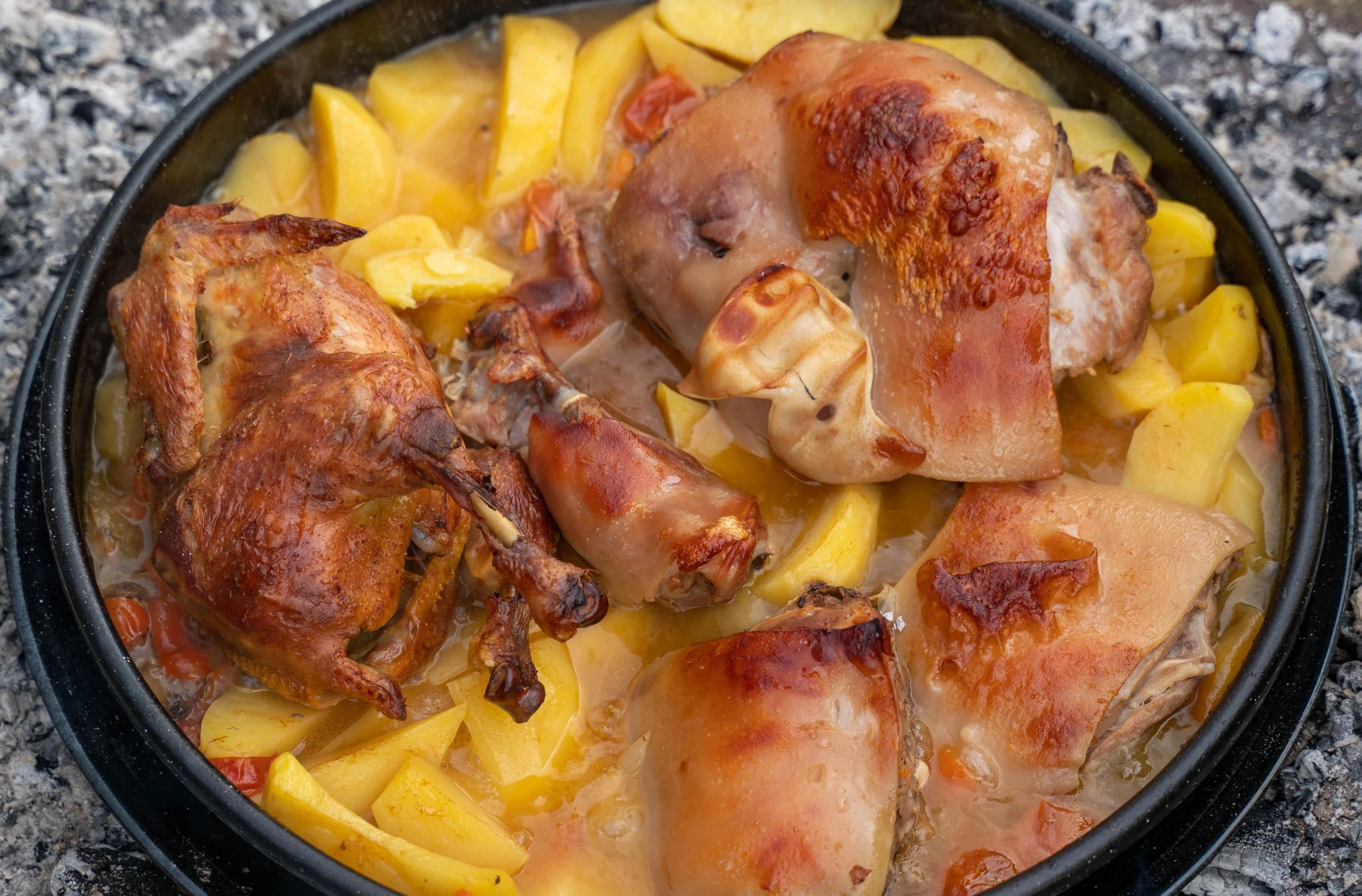 Traditional Croatian peka, featuring roasted meat and potatoes slow-cooked under a bell-shaped dome over hot embers.