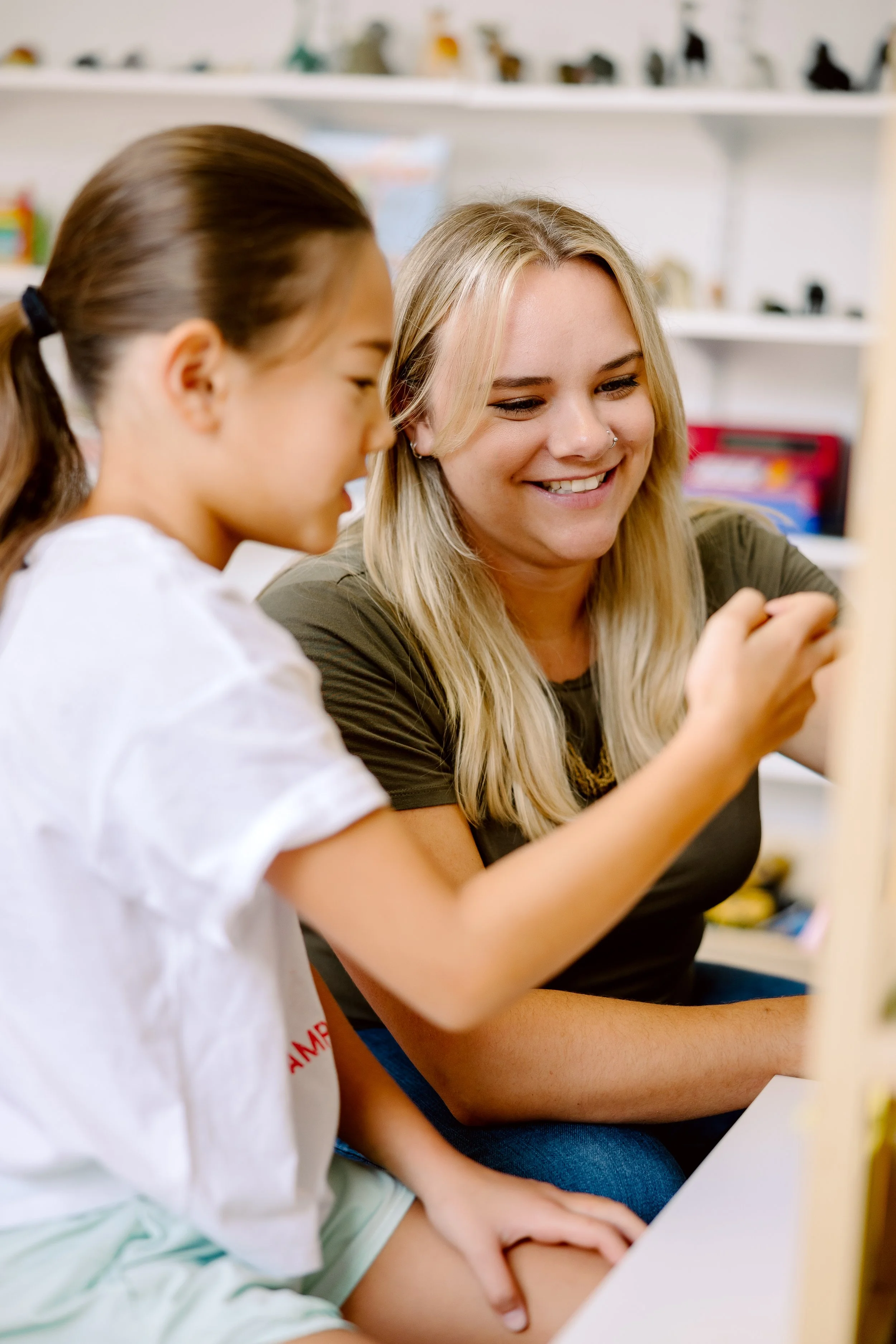 A young girl smiling and playing with a woman sitting on the floor.