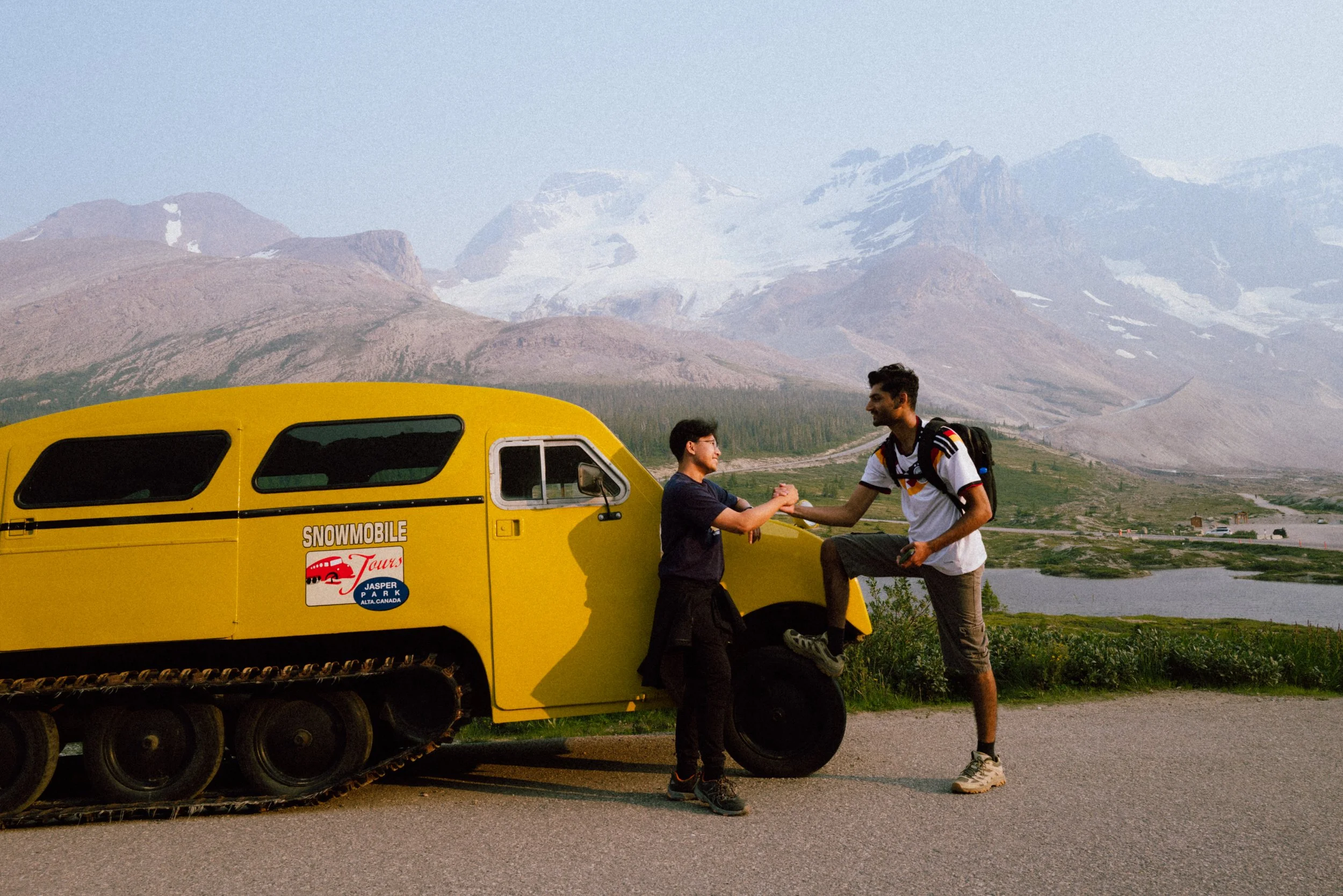 Two people shaking hands next to a yellow snowmobile with a mountain landscape in the background.