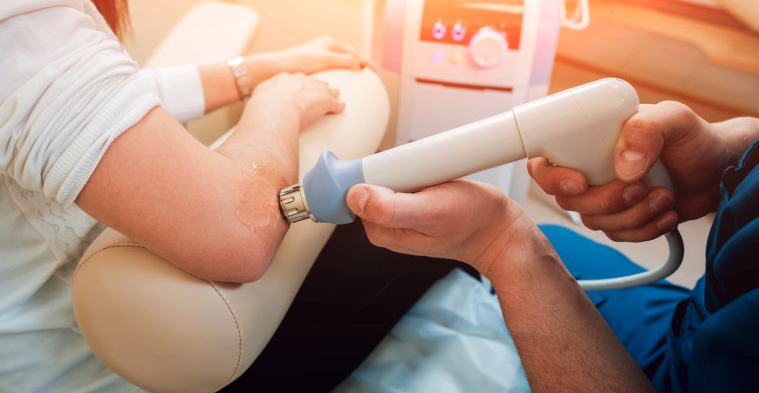 Medical professional performing ultrasound therapy on patient's elbow in clinical setting.