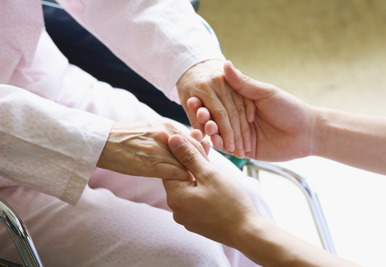 Two people holding hands, one older and one younger, in a caring gesture.