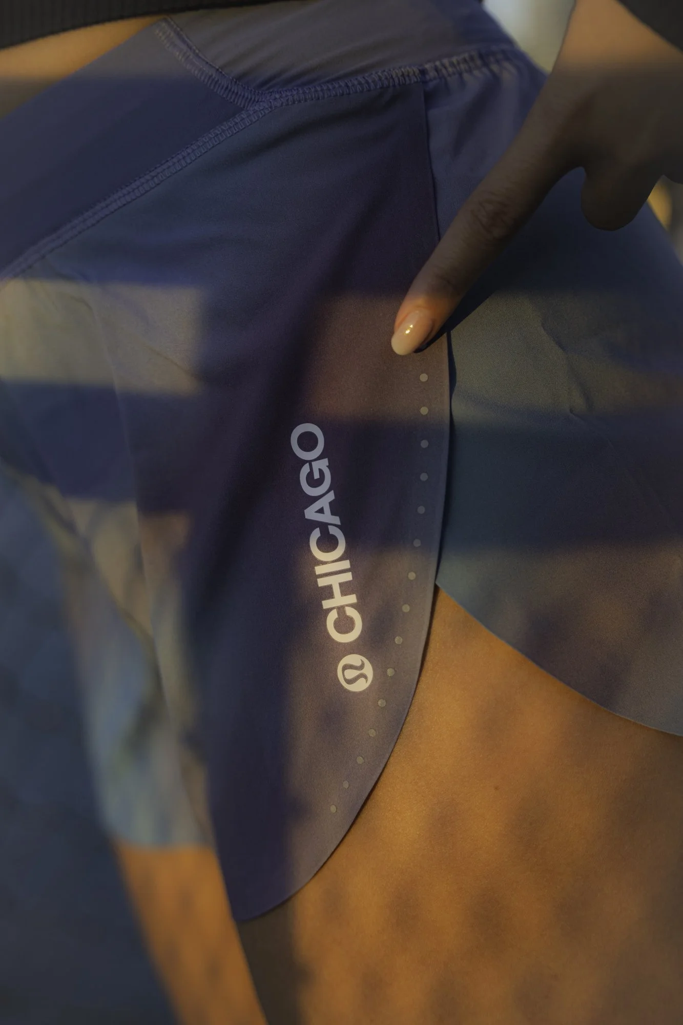 Close-up of a person wearing blue workout shorts with a Chicago logo, pointing to the side of the shorts with their finger.