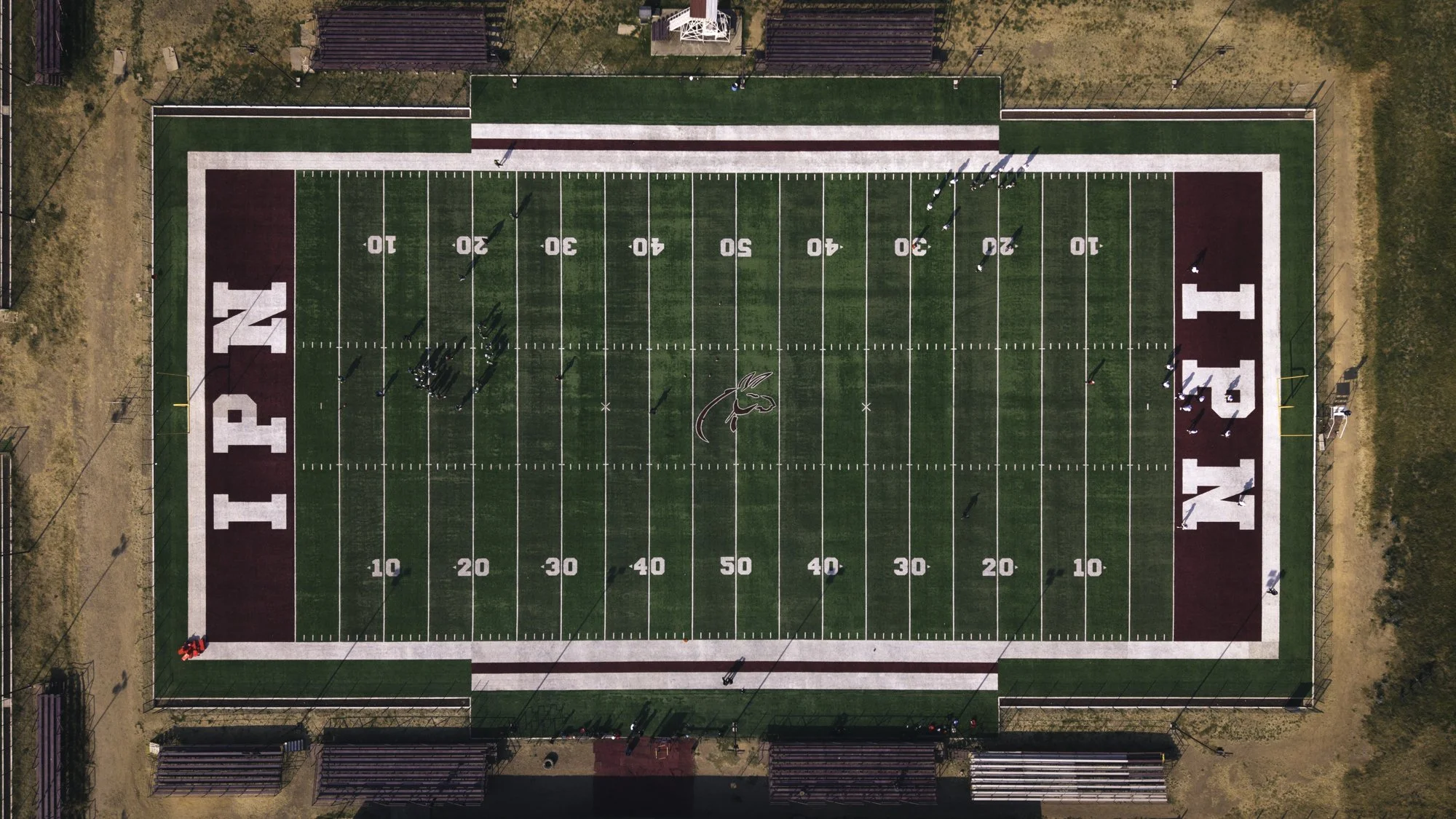 An aerial view of a football field with white yard lines and markings, featuring the words 'PINK' and 'NATION' in large white letters on the maroon end zones, and a team practicing on the field.