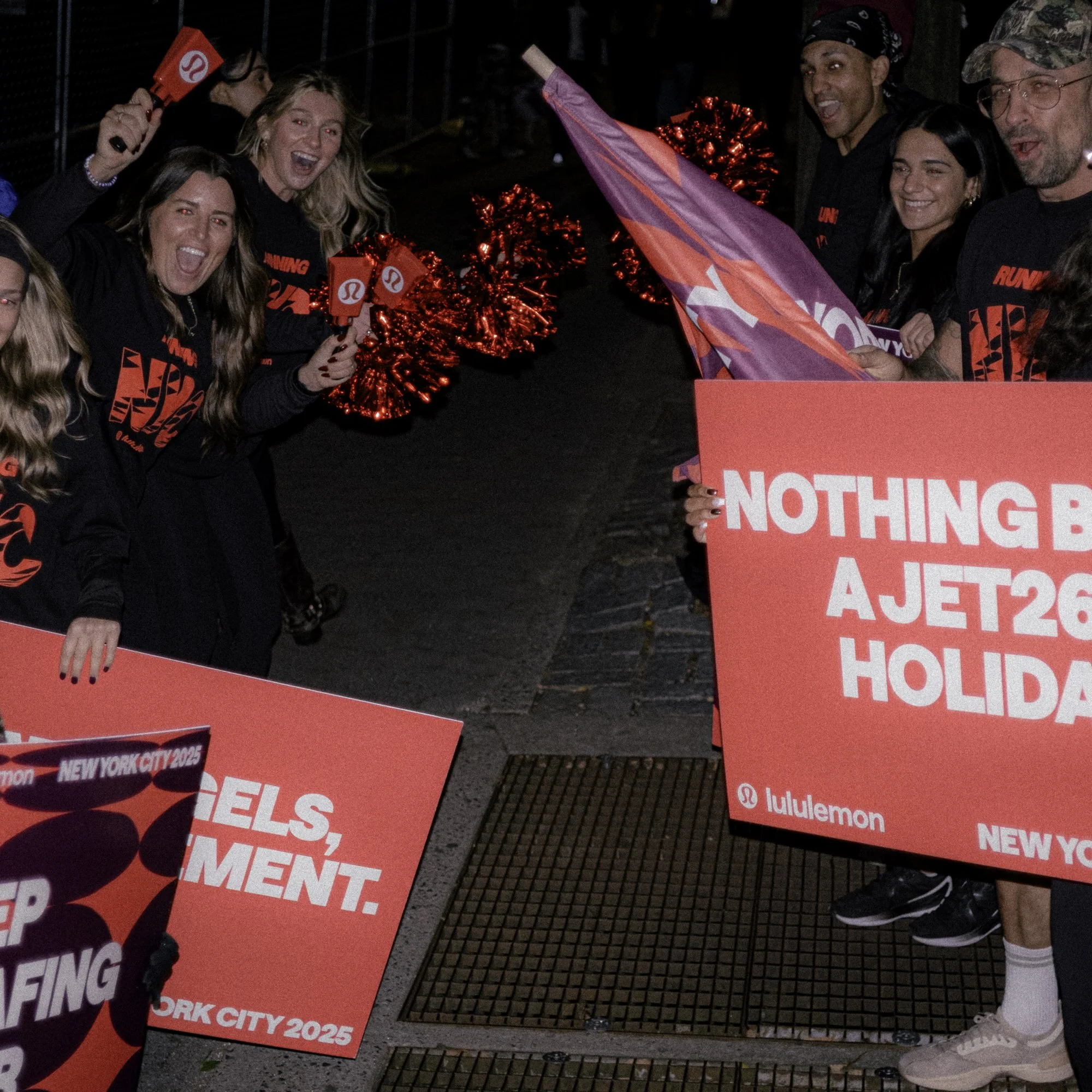 Group of smiling people holding signs and pom-poms at a parade or event, promoting Lululemon and New York City 2025.