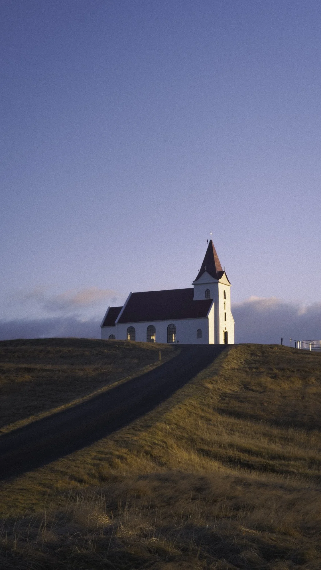 A white church with a red roof and steeple on a hill, with a clear blue sky in the background.