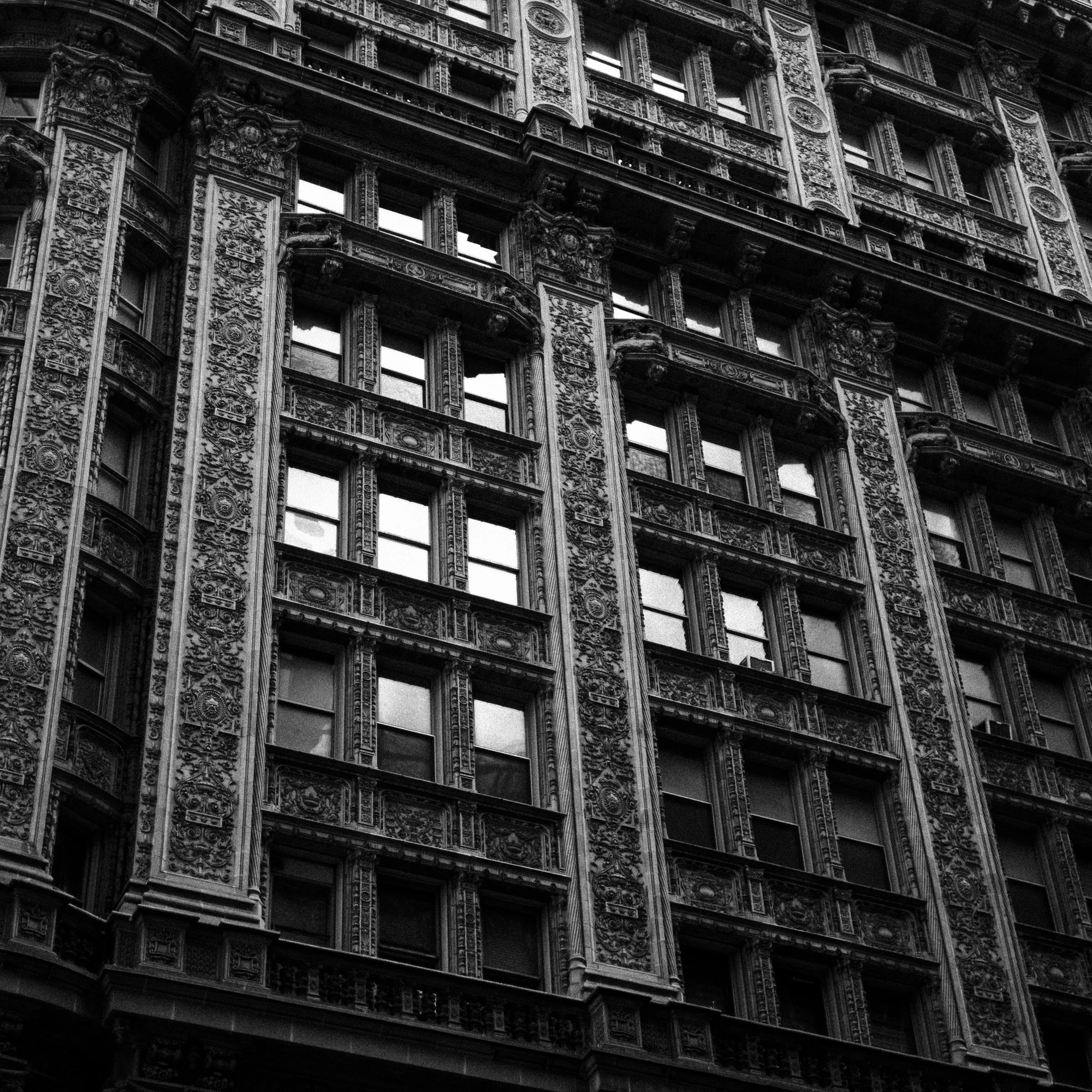 A black-and-white photograph of an ornate, historic building facade with multiple windows, detailed carvings, and architectural embellishments.