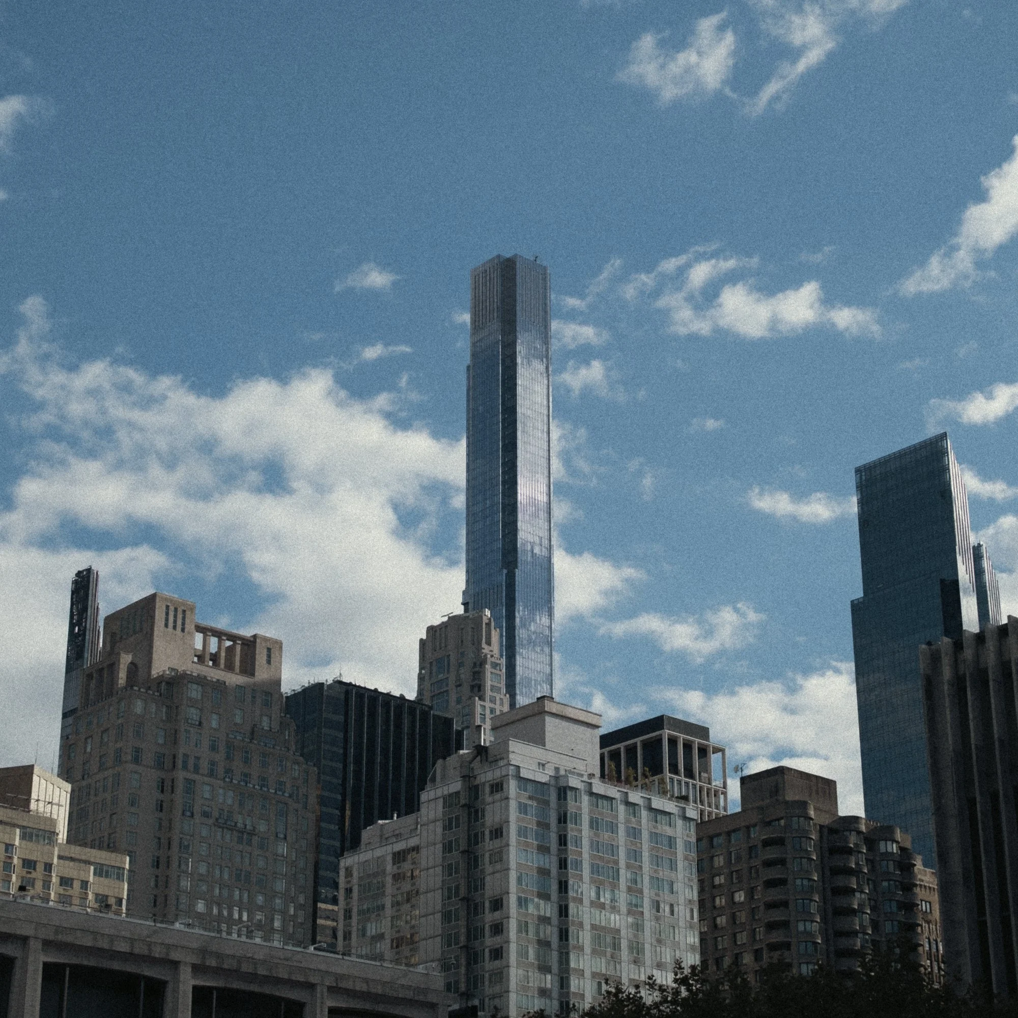 Skyline of tall skyscrapers against a blue sky with scattered white clouds.