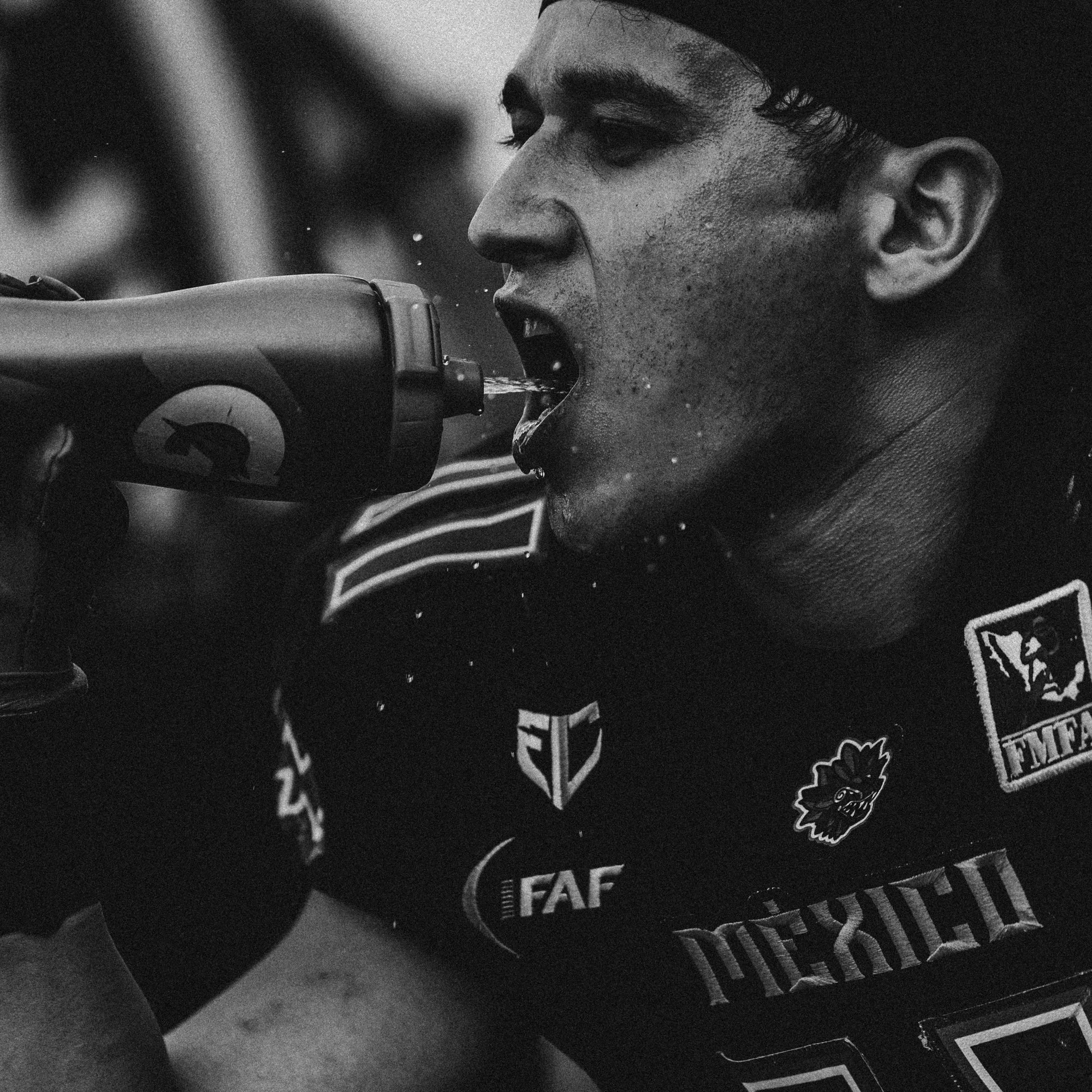 Close-up of a cyclist wearing a jersey with logos, drinking water from a bottle.