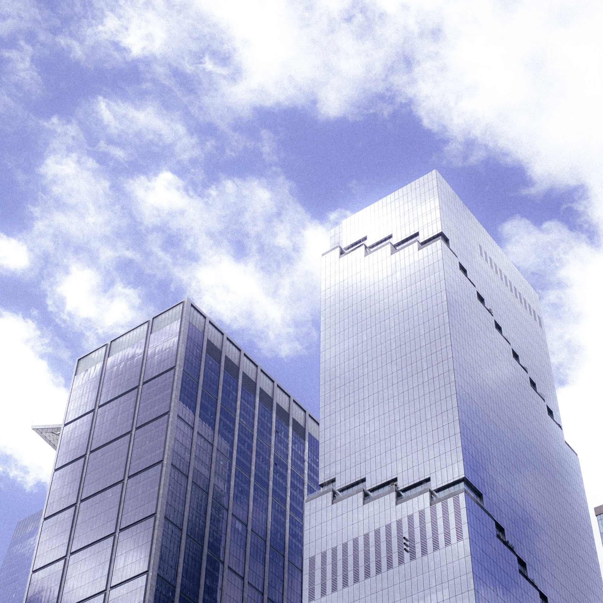 Two modern skyscrapers with glass facades against a blue sky with clouds.